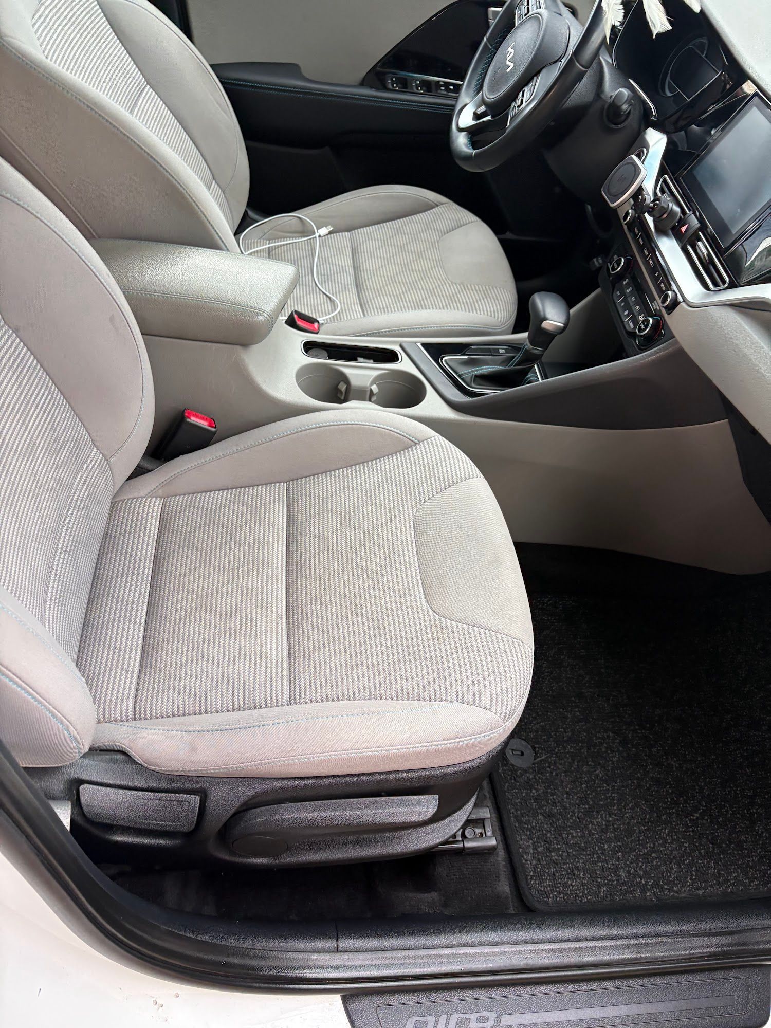 Car interior with gray fabric seats, center console with cup holders, and steering wheel.