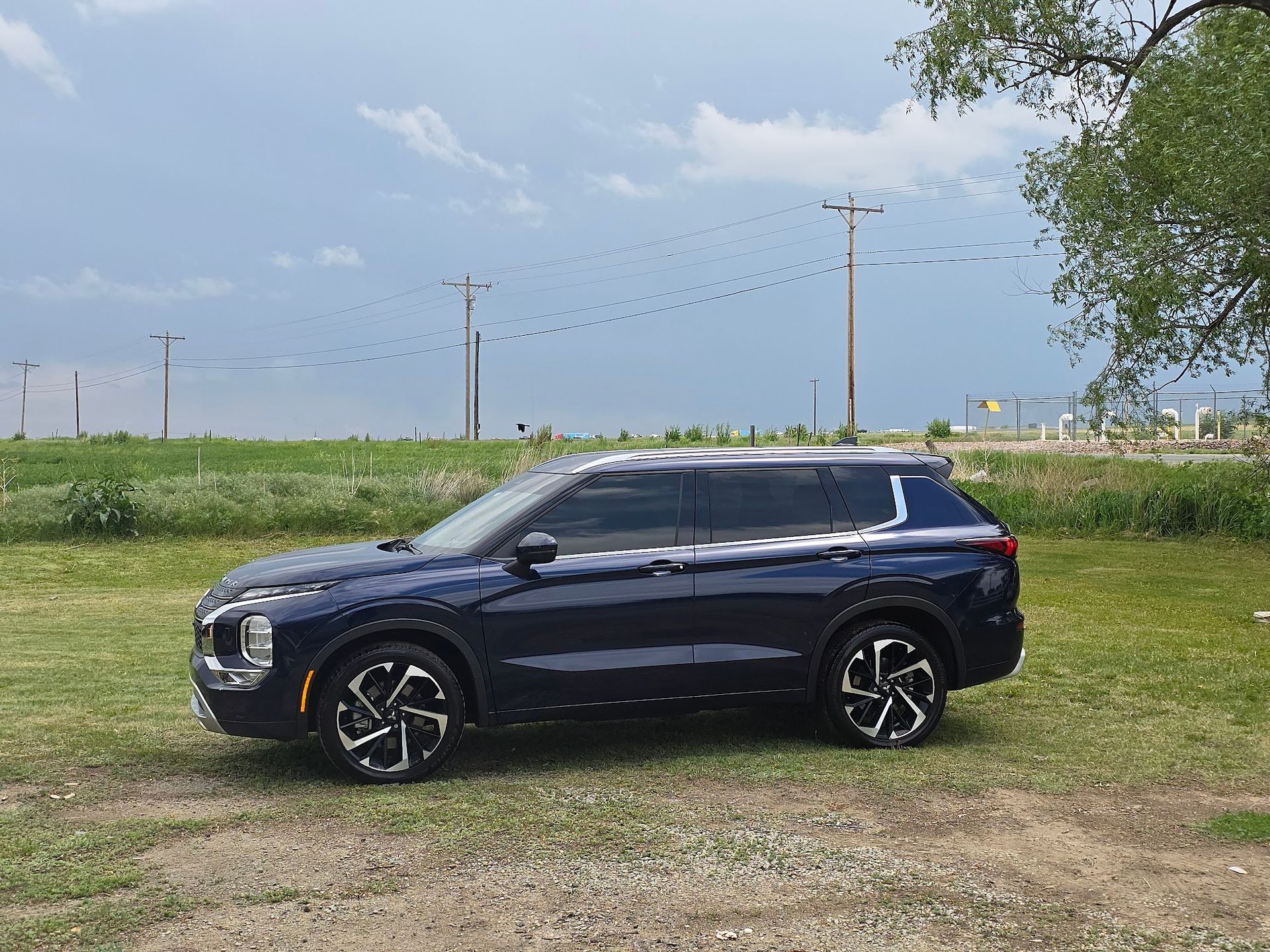 Dark blue Mitsubishi SUV parked on grass with a cloudy sky backdrop.