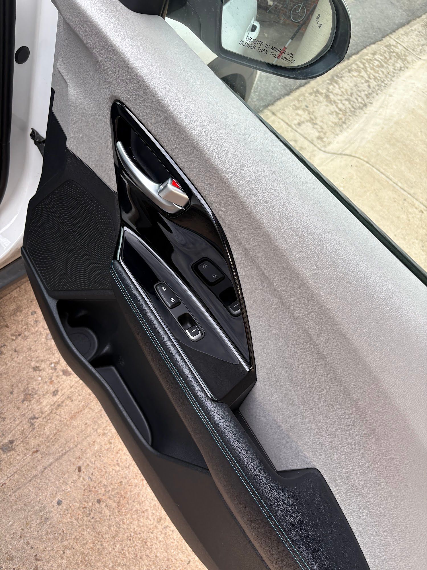Car door interior: Black handle, glossy black trim with window controls, gray fabric panel, cup holder.