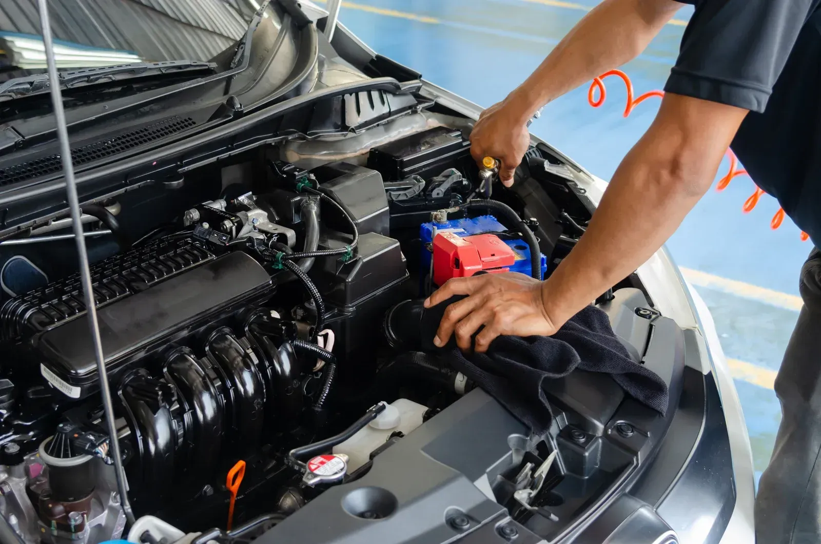 Mechanic working on a car engine with tools; engine compartment, light blue wall in the background.