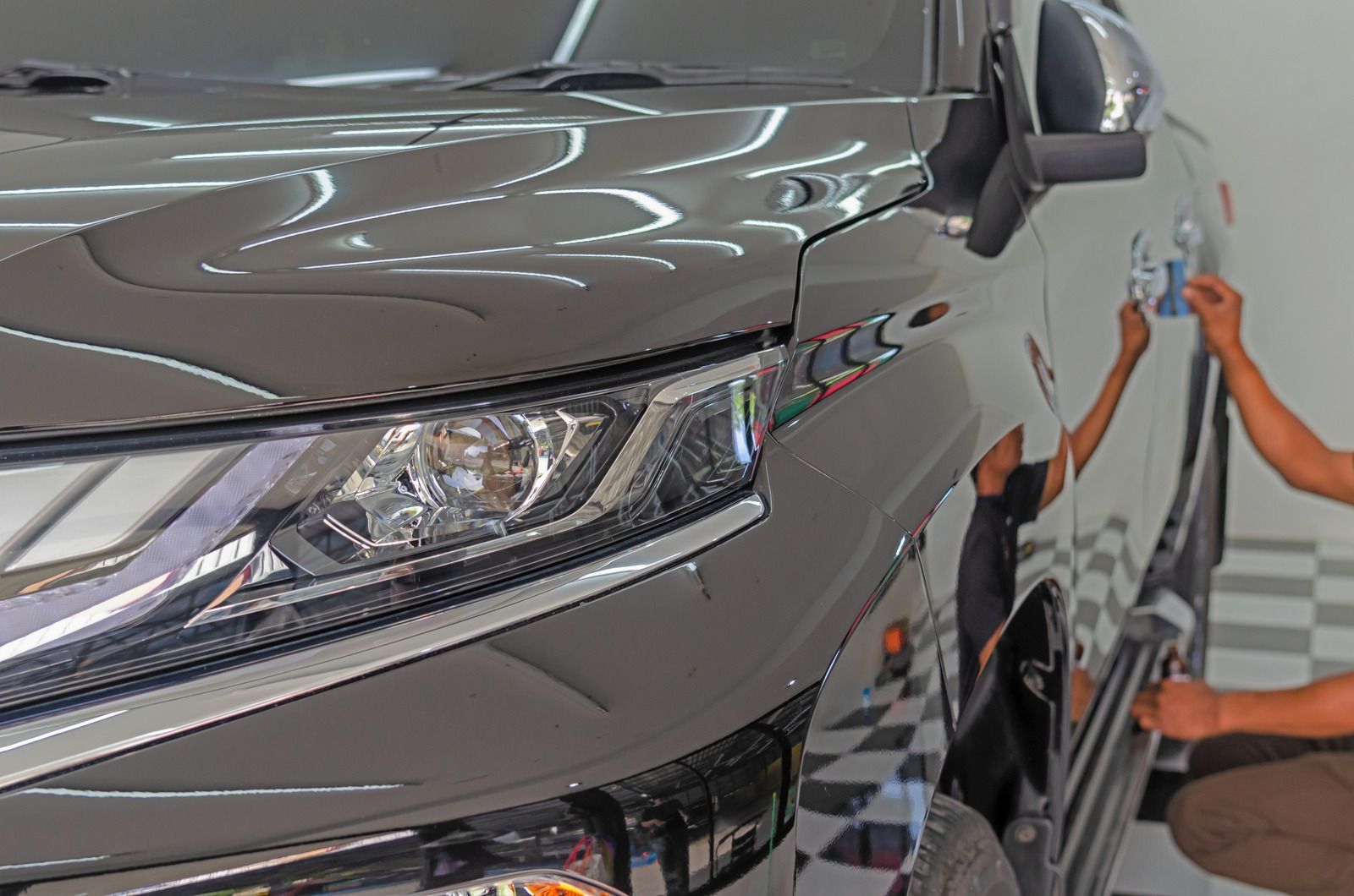Person polishing a shiny black car; bright reflections on the polished surface, indoors.