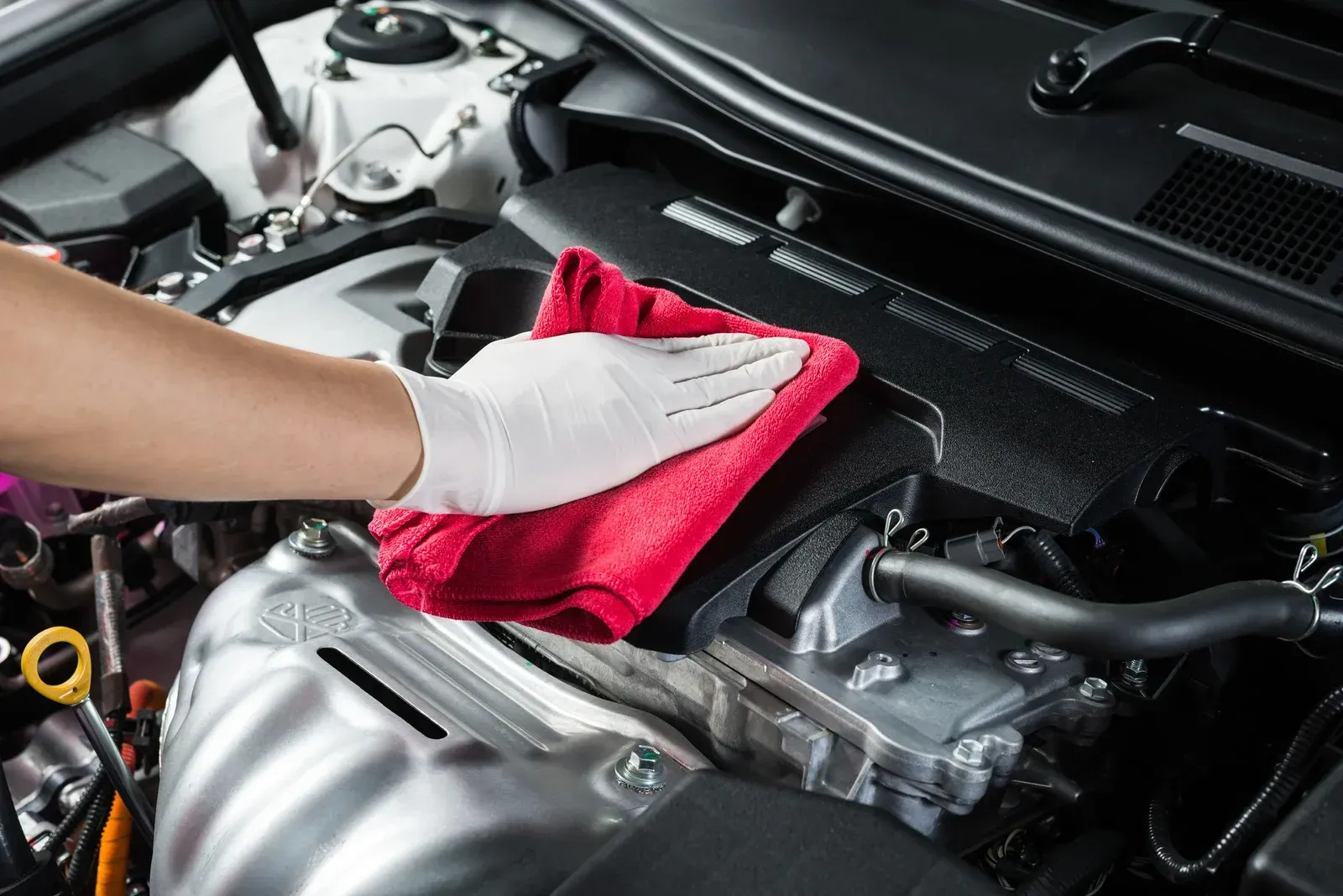 Hand cleaning a car engine with a red cloth.