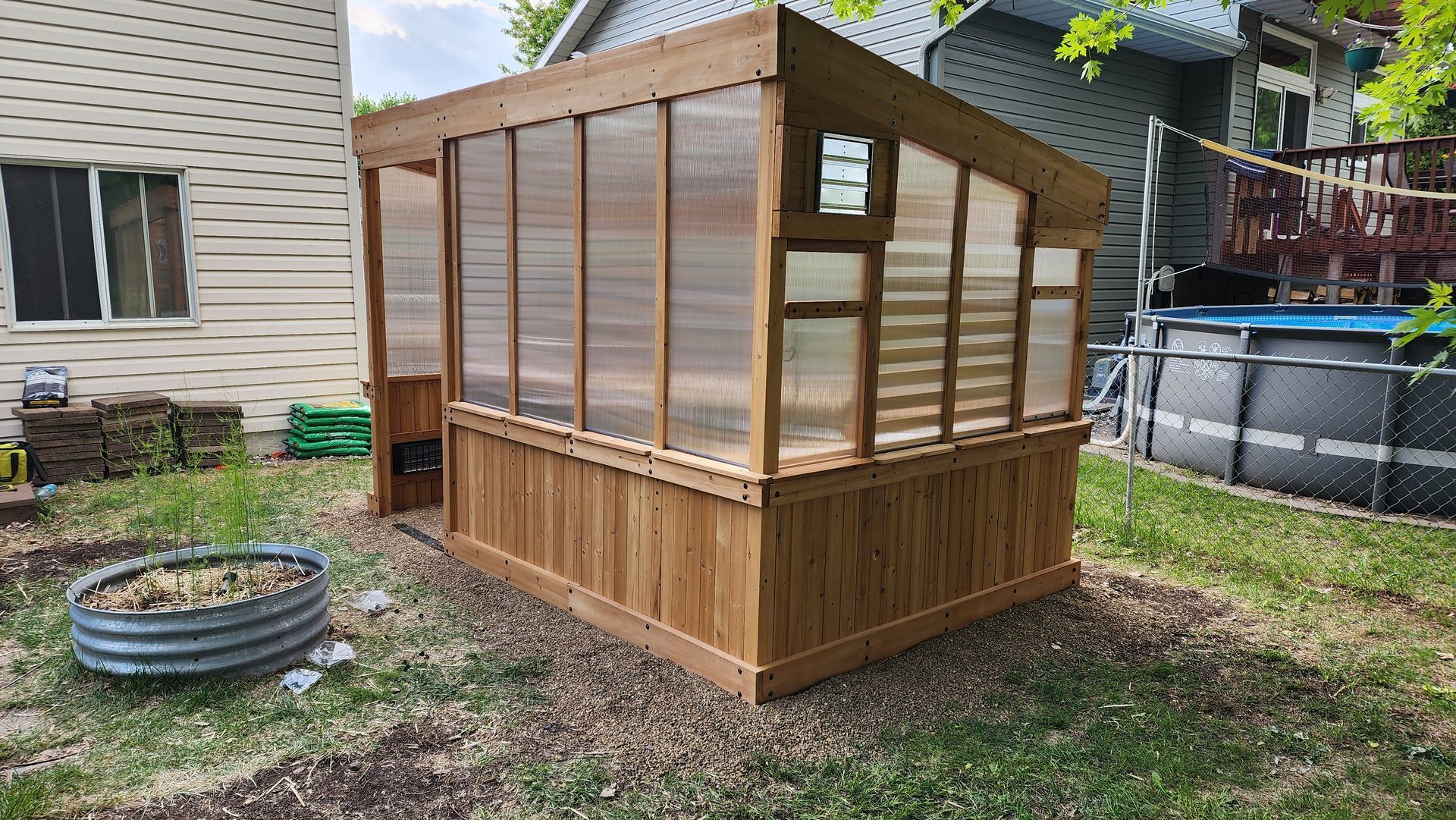 Wooden greenhouse with translucent panels, in a backyard setting.