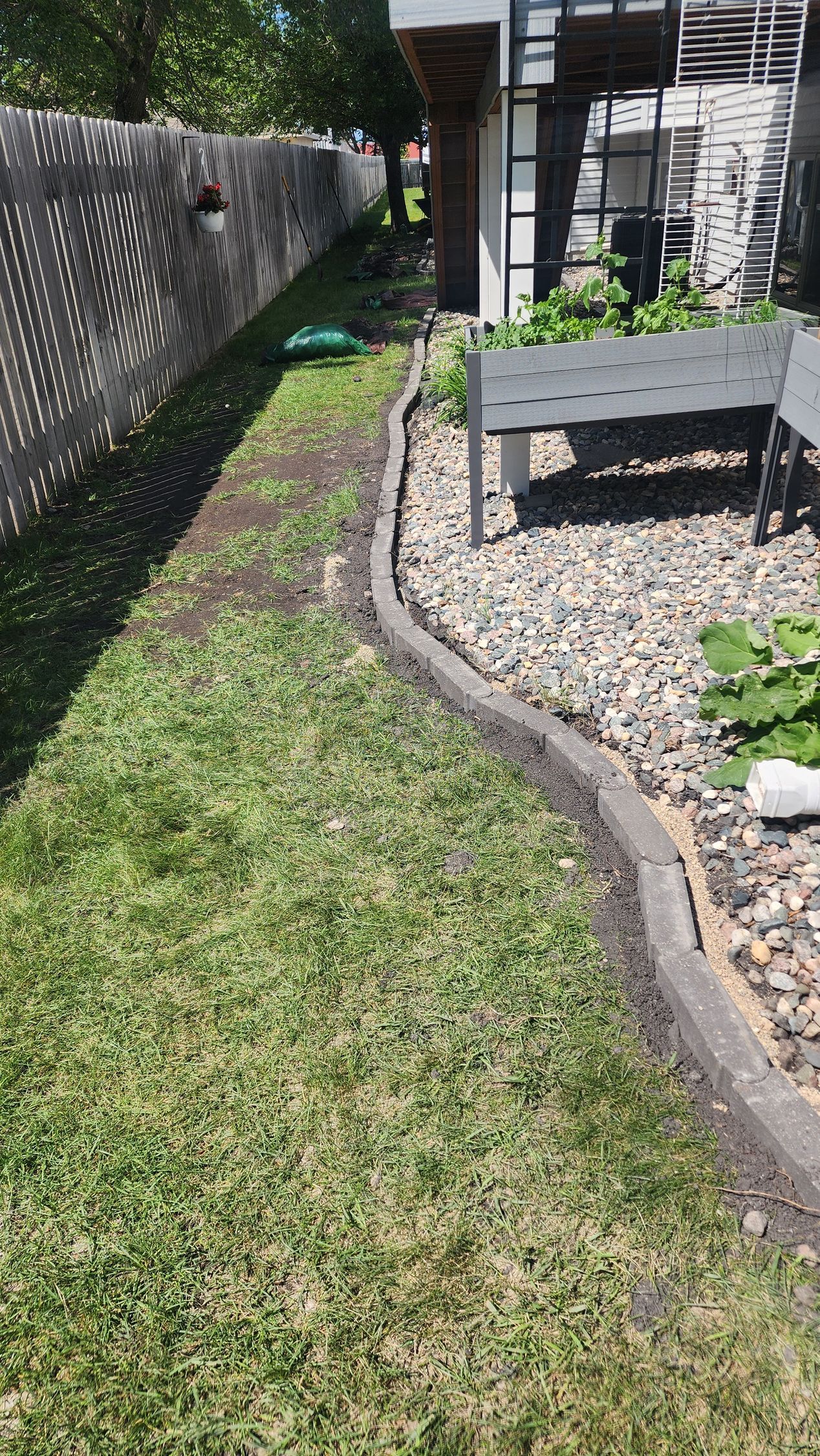 Green grass bordering a concrete curb along a fence and gravel area.