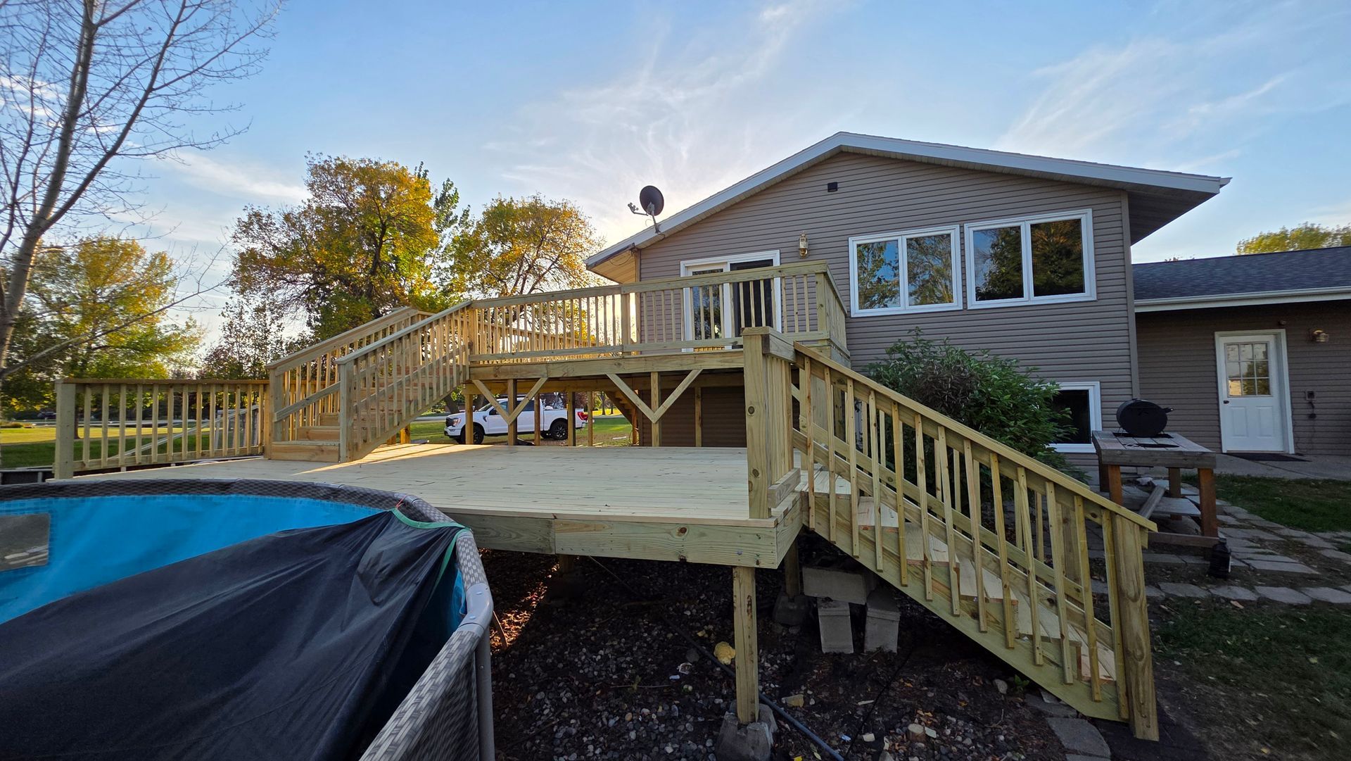 Wooden deck with stairs attached to a house with an above-ground pool visible in the foreground.