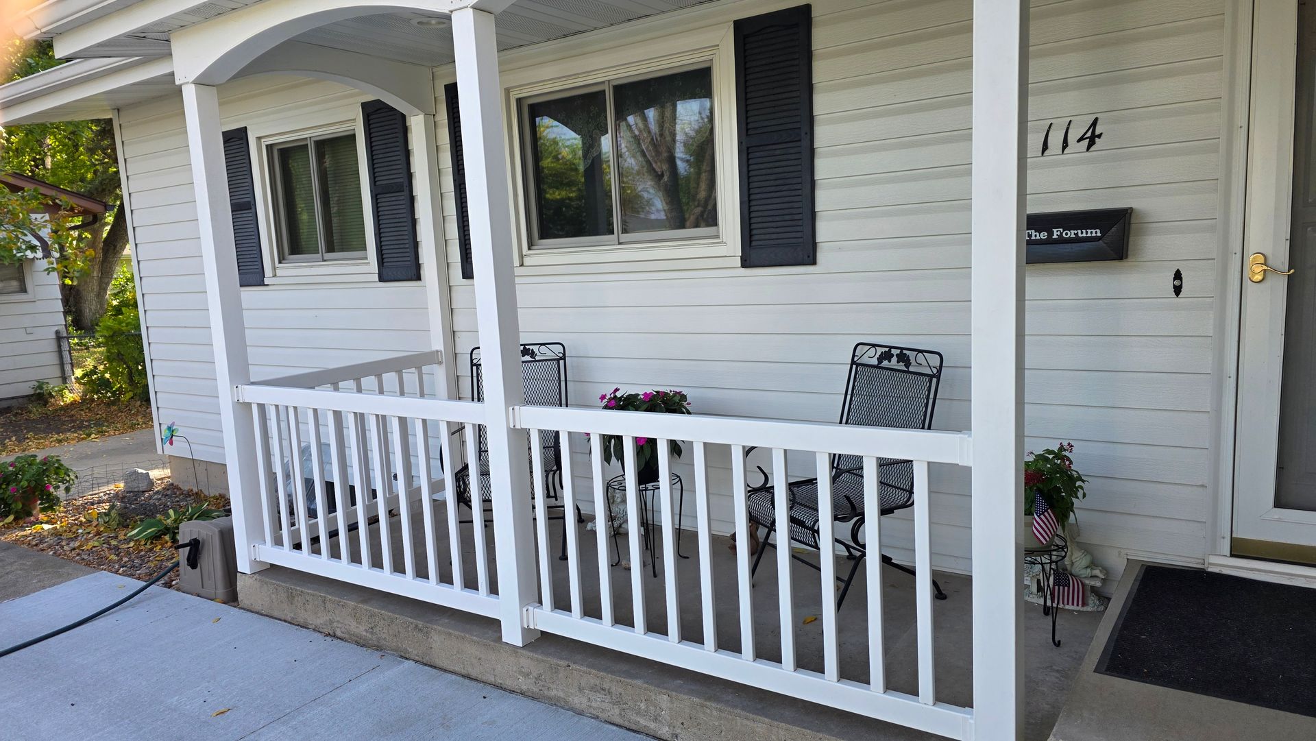 White porch with railing, two chairs, and a front door. House number 114 above the mailbox.