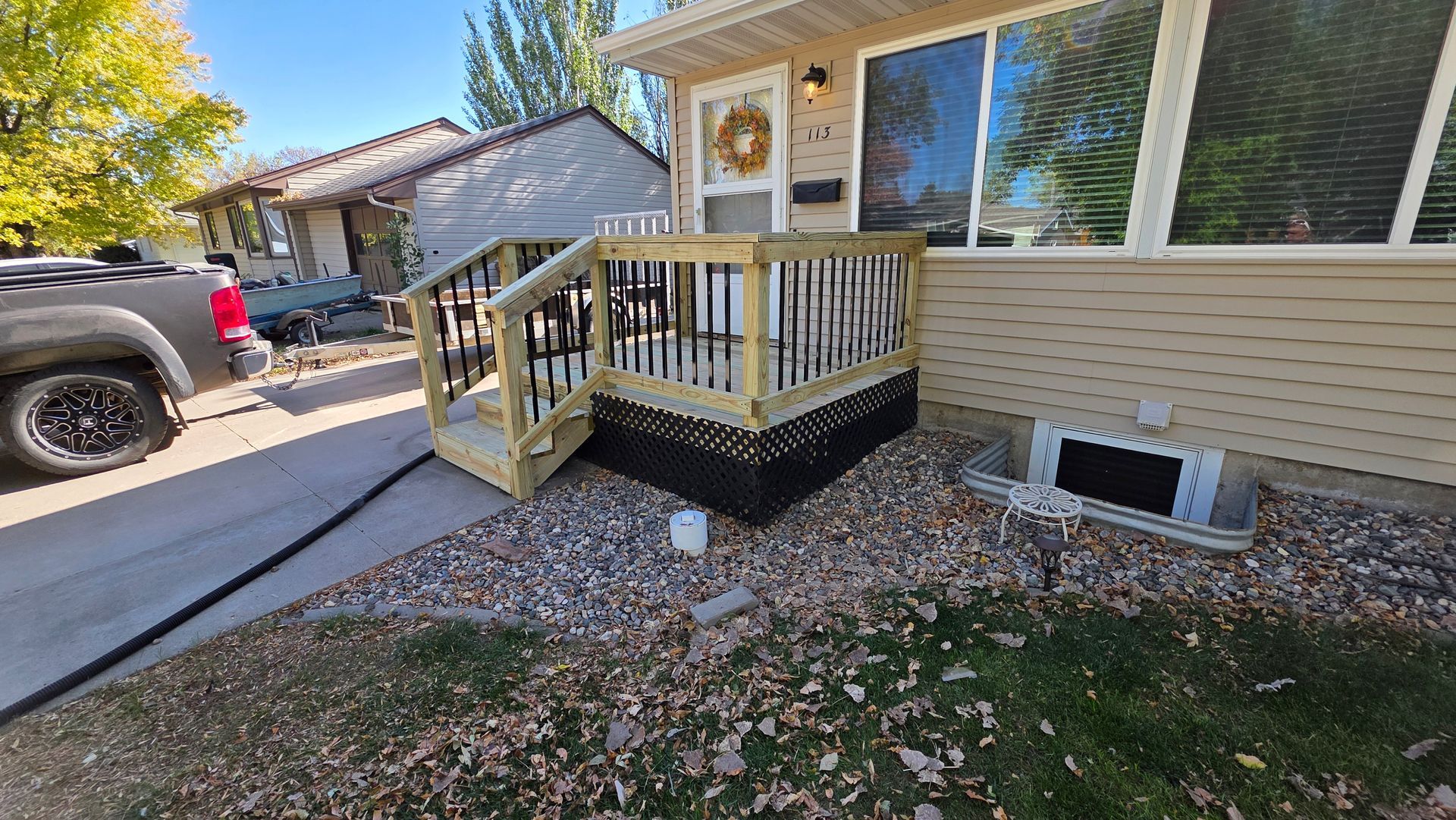 New wooden porch with black railing and steps in front of a tan house.