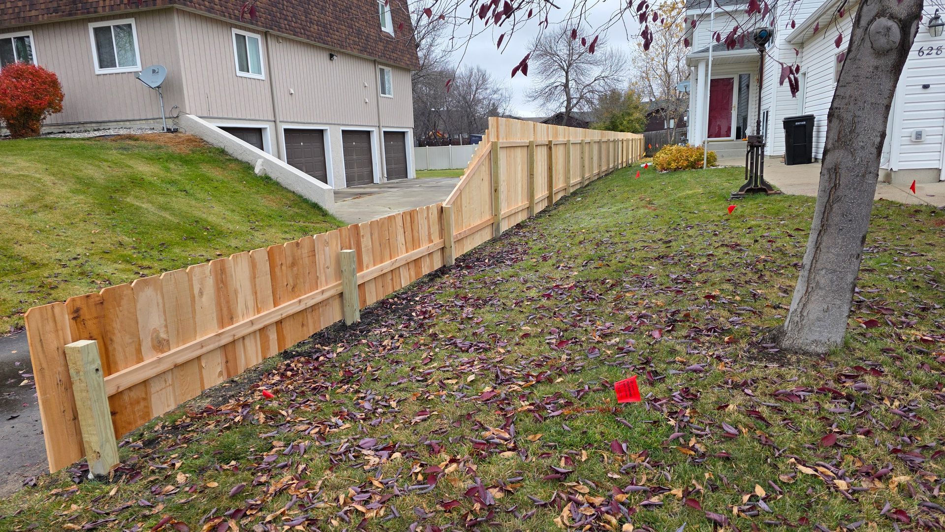 Wooden fence bordering a grassy hill beside a building and sidewalk.