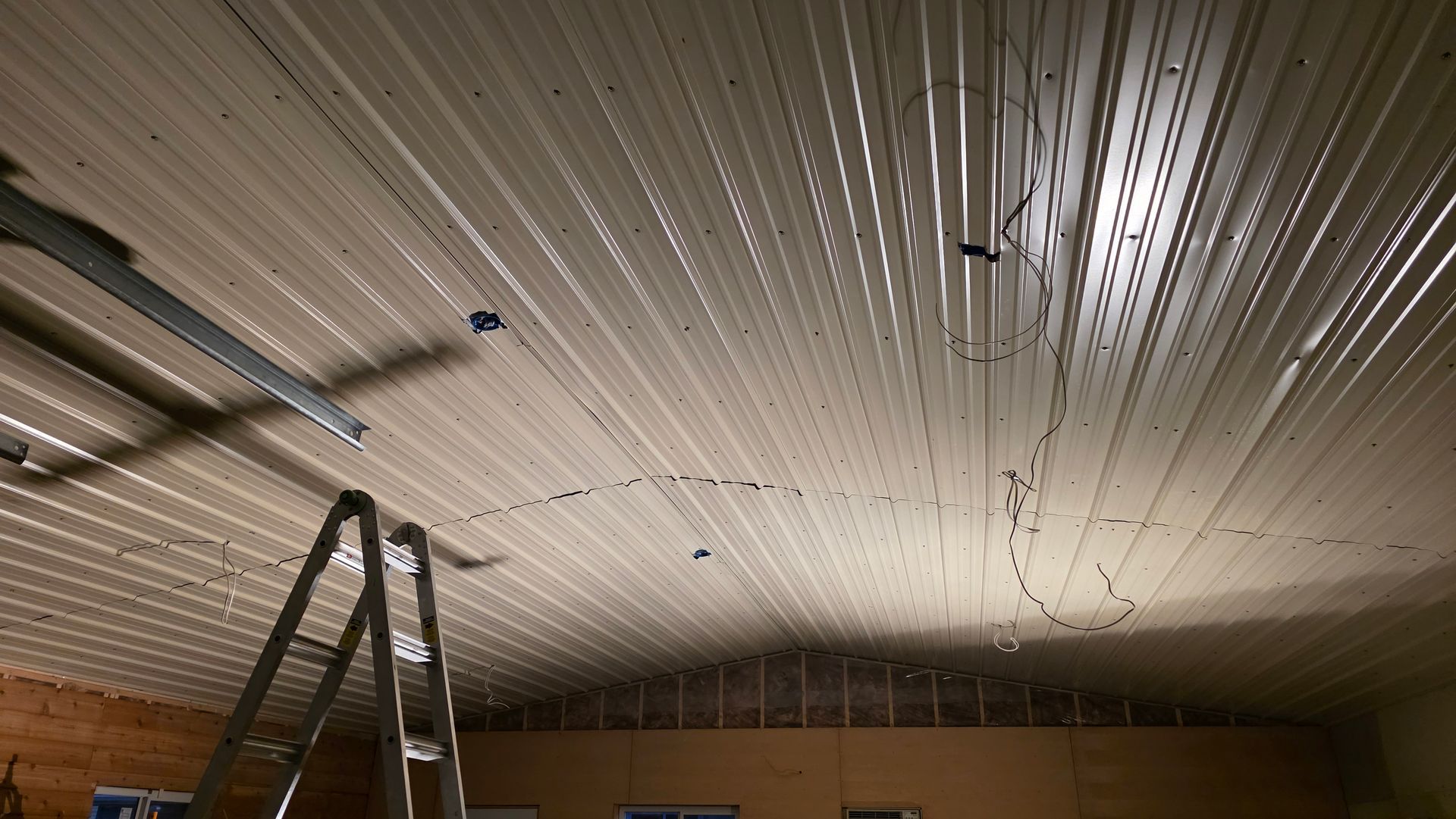 Metal ceiling with exposed wiring, ladder, and partially visible garage door frame in a building.