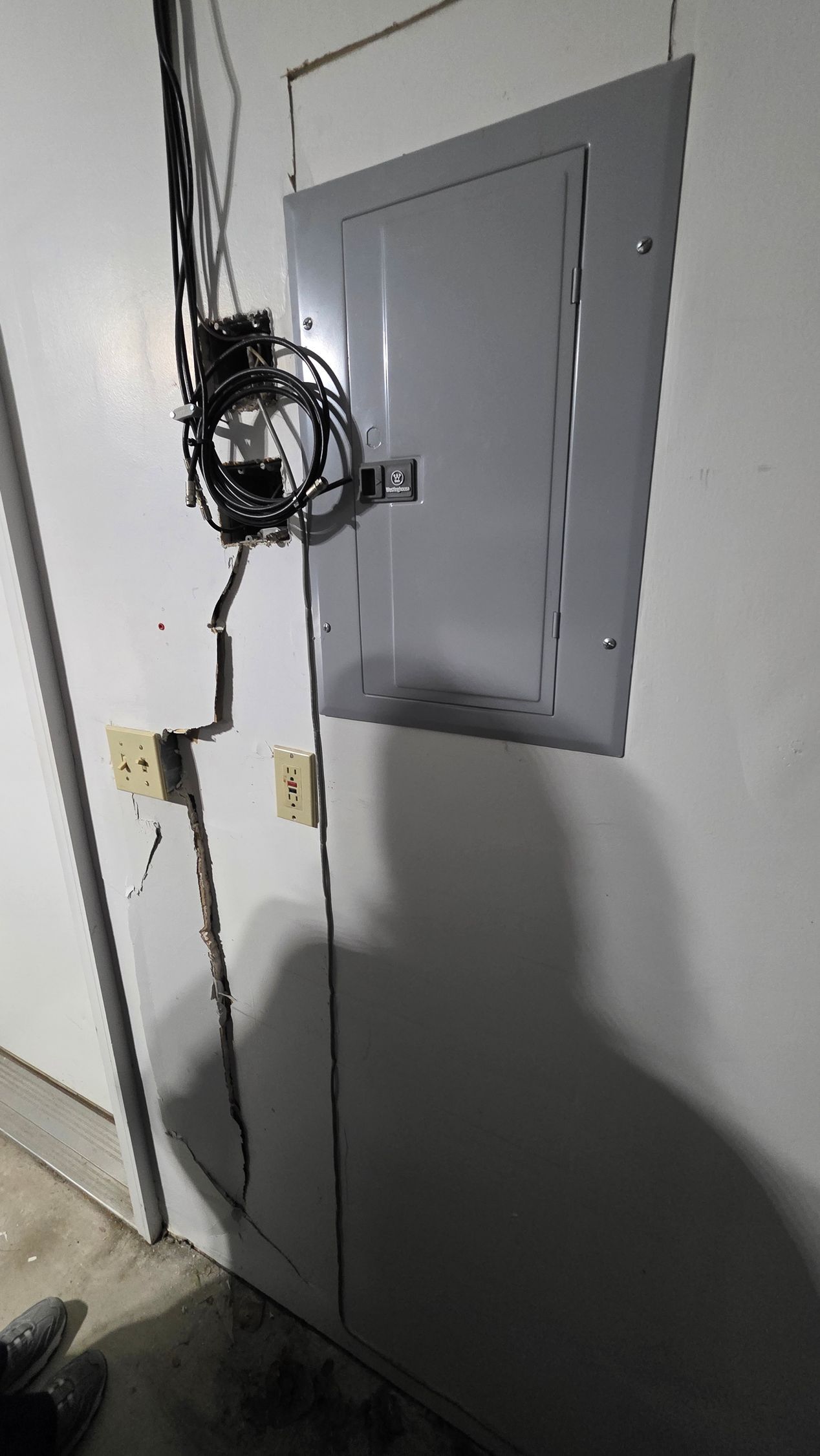 Electrical panel on white wall with tangled wires and two outlets.