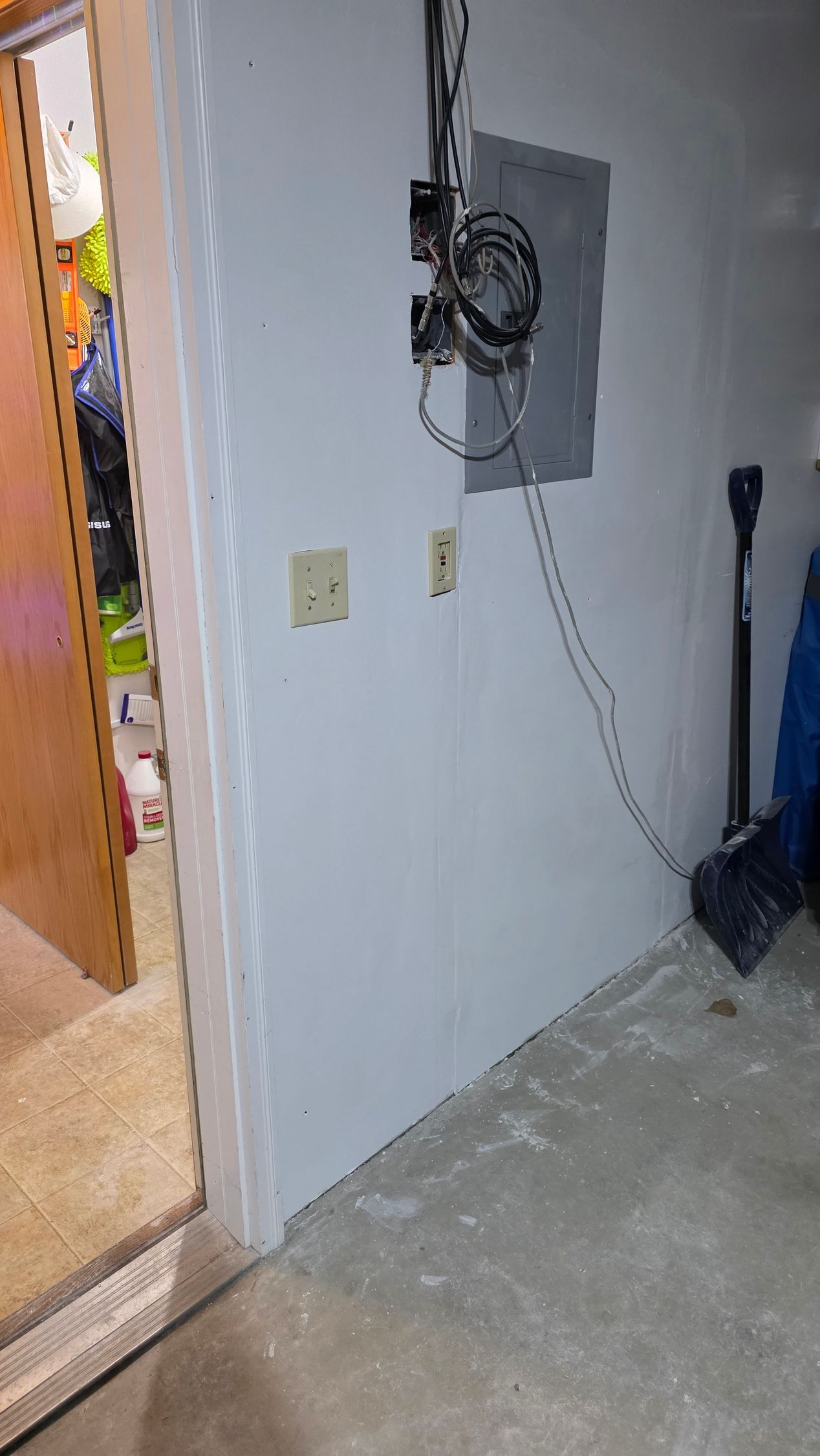 White painted wall with electrical panel and outlets; doorway to storage area on left.