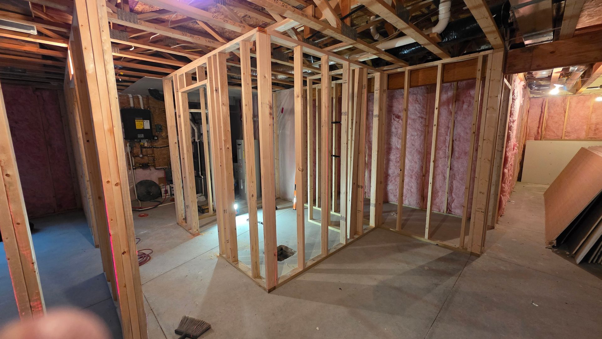 Interior basement framing of a room and closet. Exposed wood studs, pink insulation, unfinished concrete floor.