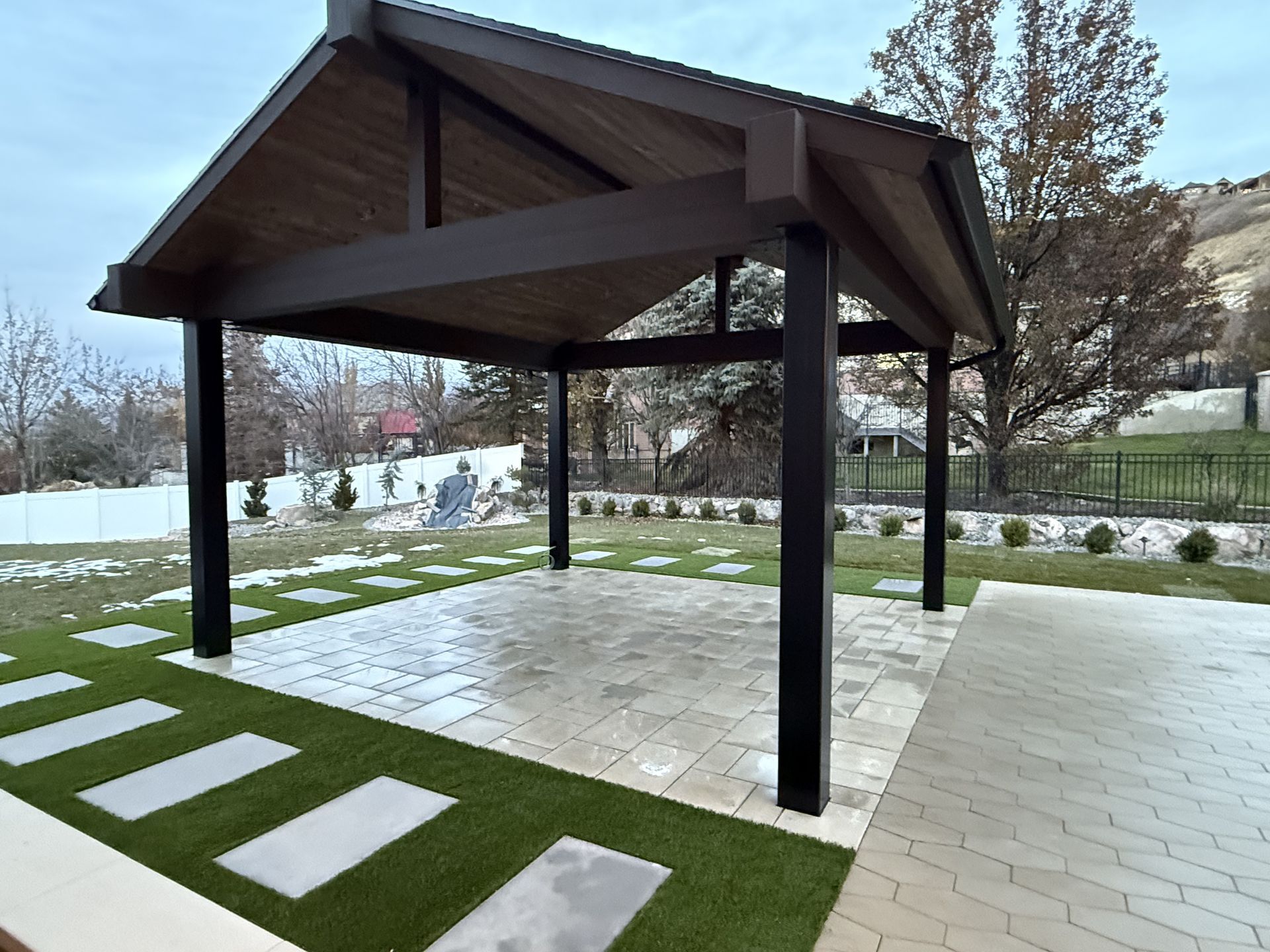 A wooden gazebo with a roof is sitting on top of a lush green lawn.
