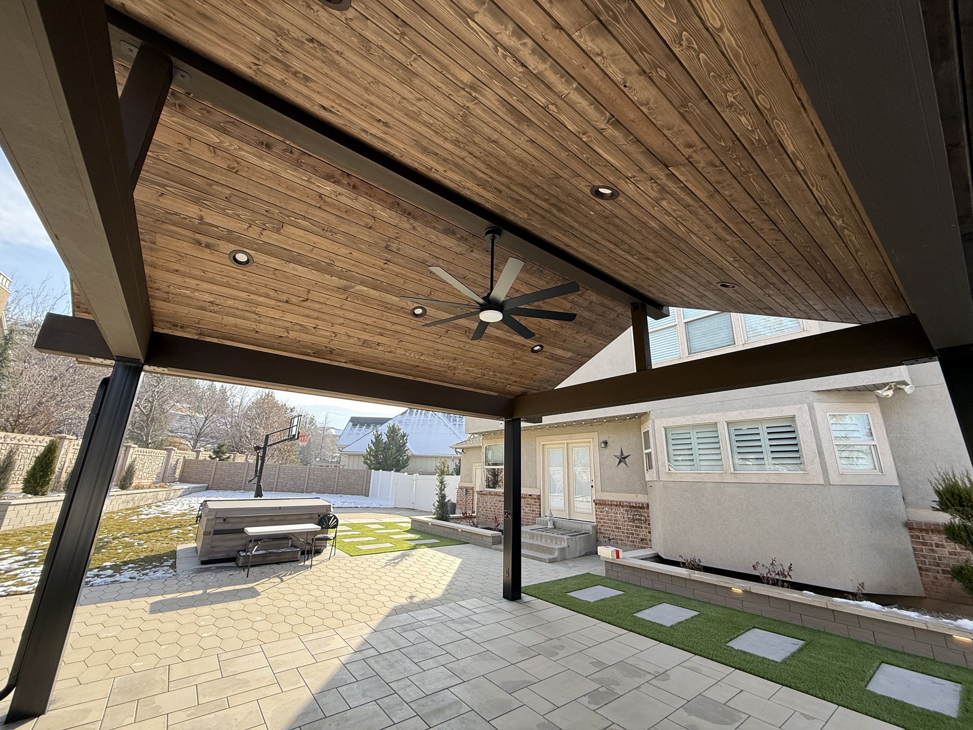 A patio with a wooden ceiling and a ceiling fan.