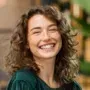 A woman with curly hair is smiling and wearing a green shirt.
