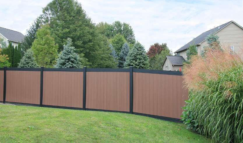Wooden privacy fence along a grassy backyard with trees and houses in the background