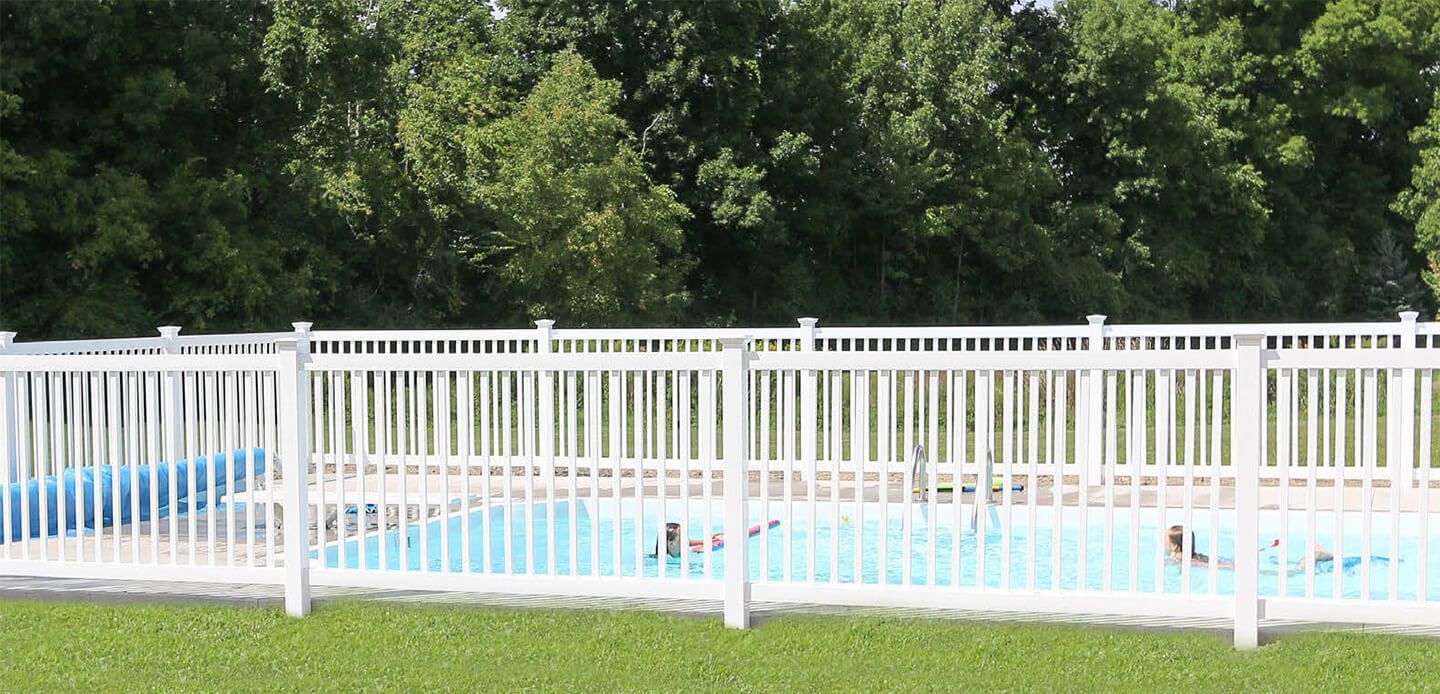 White fence around a blue pool with trees in the background