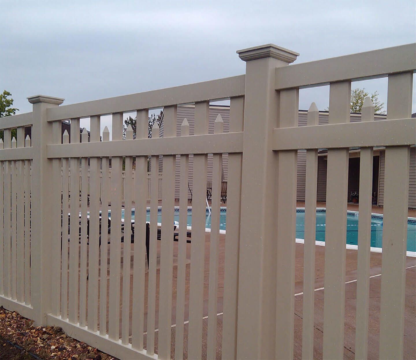 Beige metal fence with vertical slats in front of a swimming pool and building