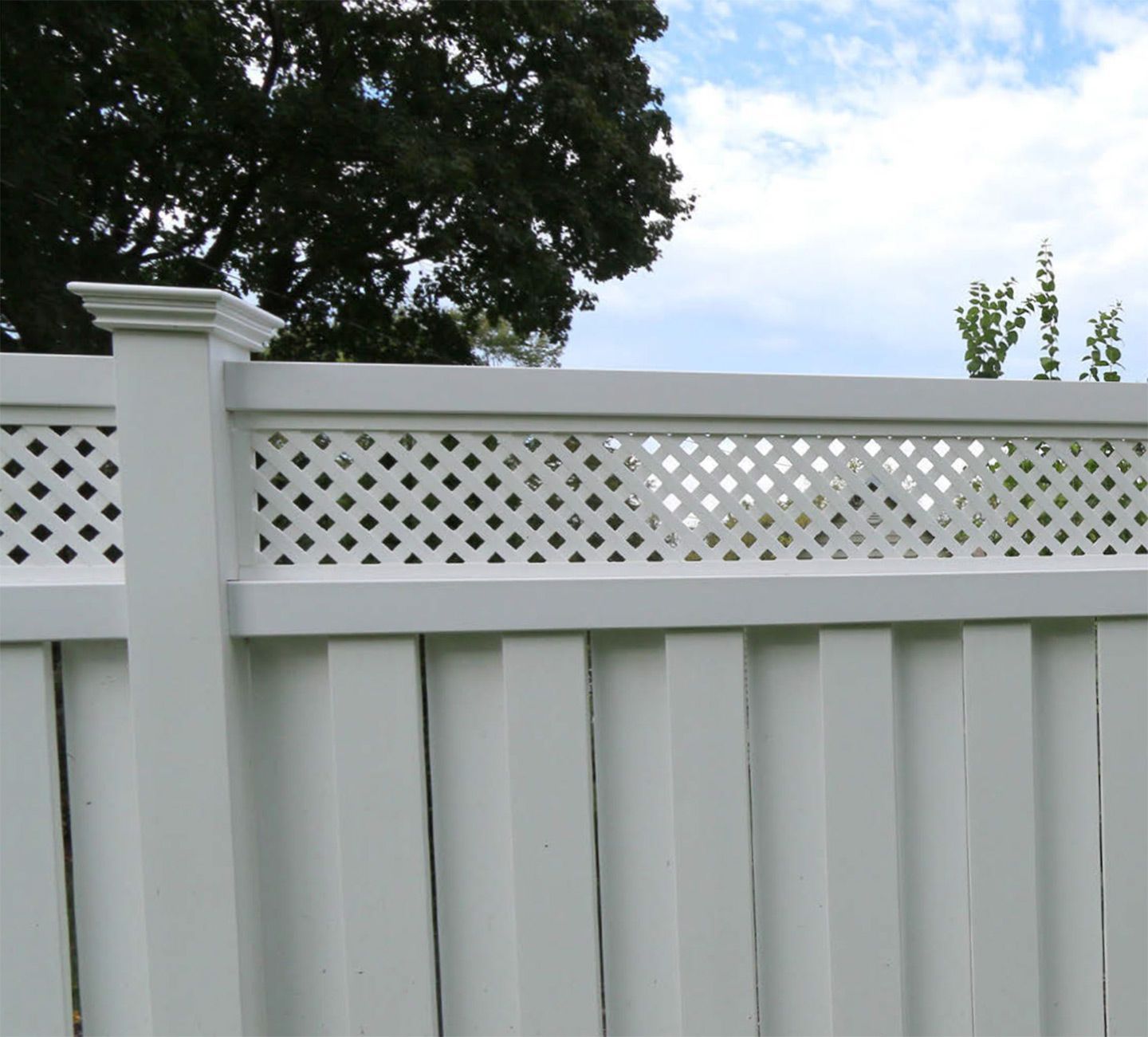 White vinyl fence with lattice top under a partly cloudy sky