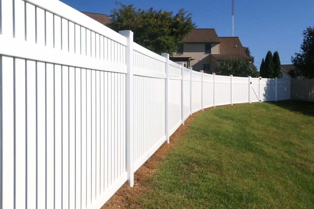 White vinyl fence along a grassy yard under a clear blue sky