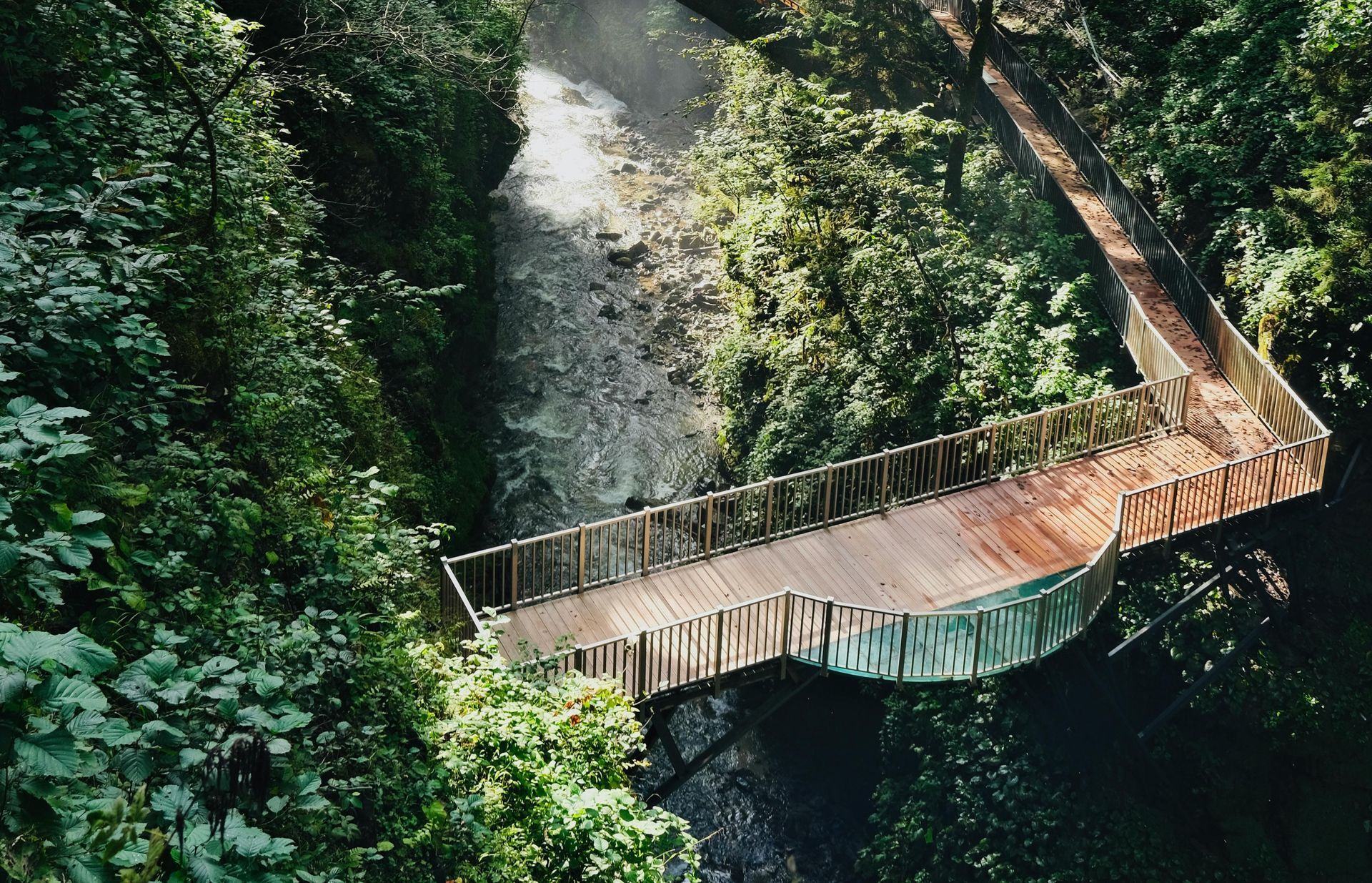 Wooden bridge over a river canyon, surrounded by dense green foliage.