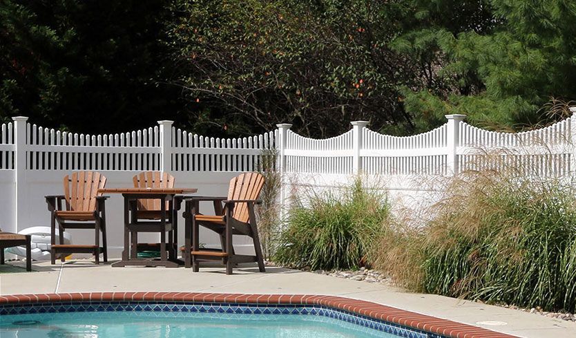 Backyard patio with table and chairs beside a swimming pool and white fence