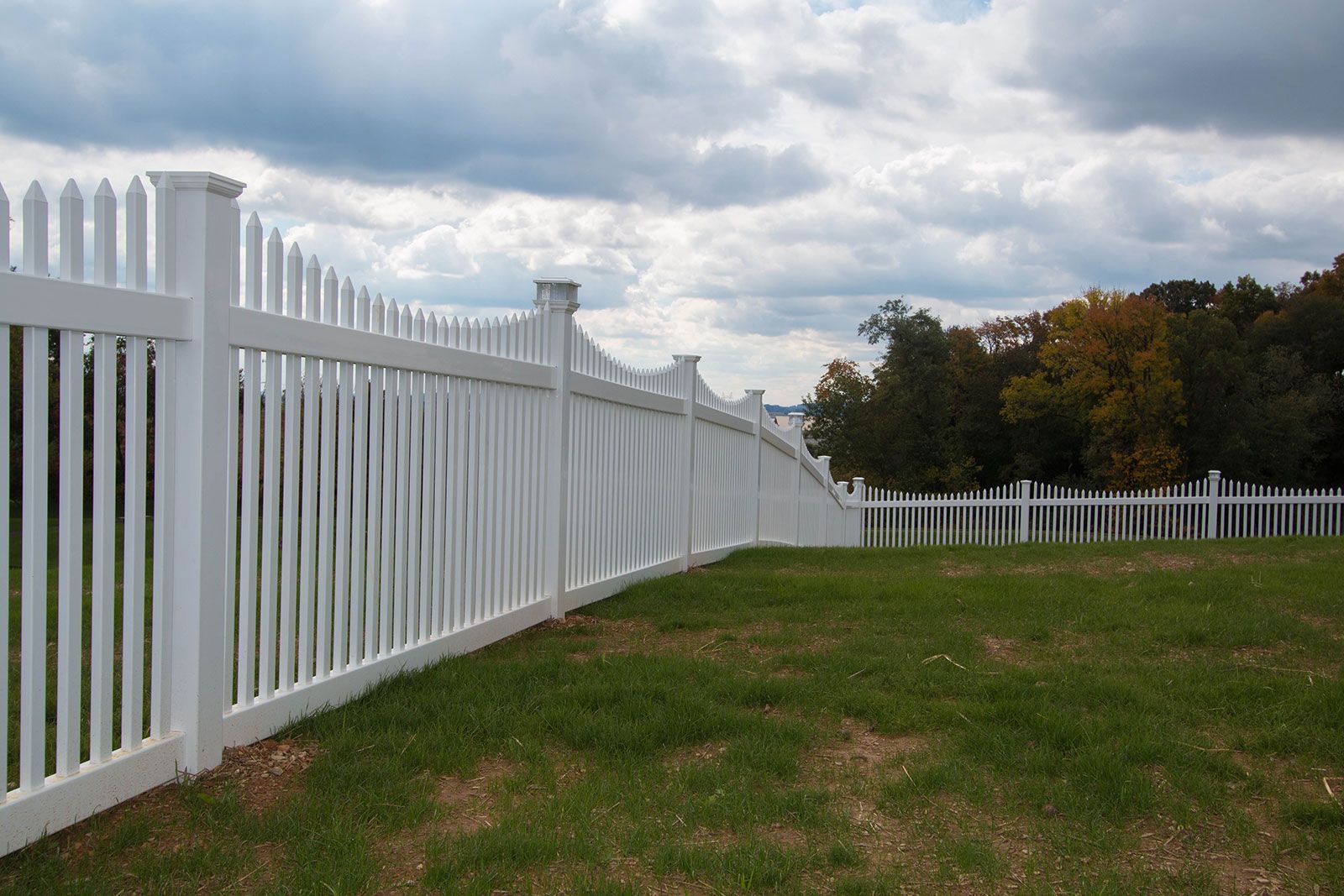 White picket fence curving along a grassy field under a cloudy sky