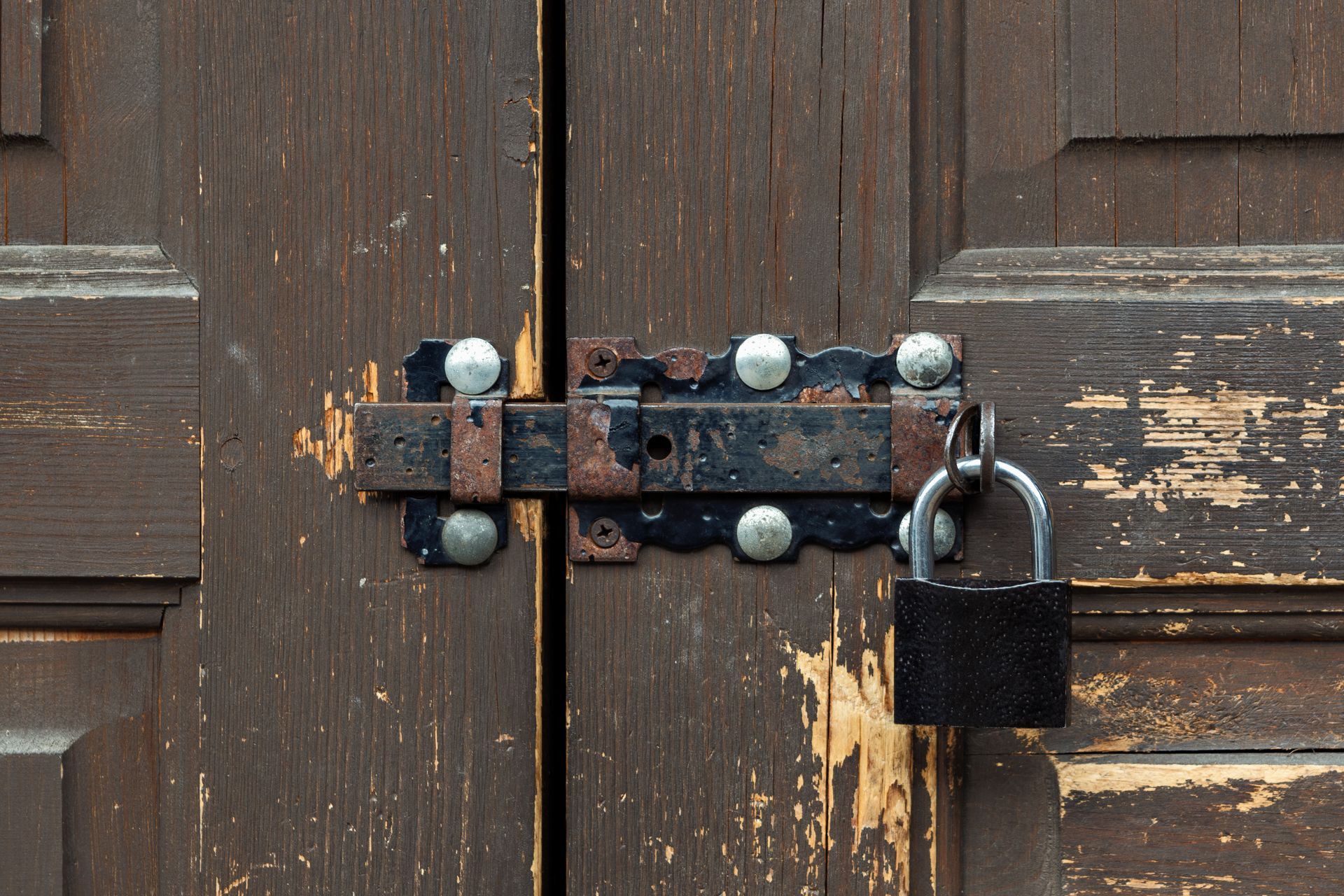 Rusty metal bolt and padlock securing a weathered wooden door in State College