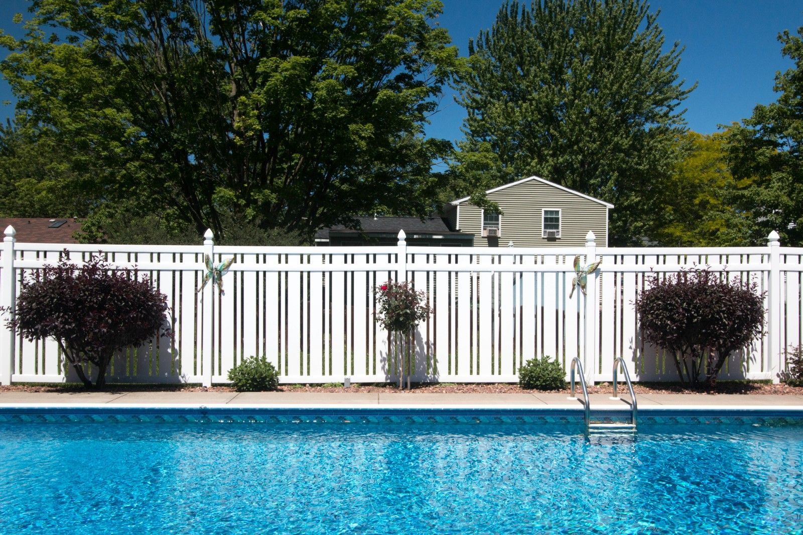 Blue pool in front of a white fence and trees under a clear sky