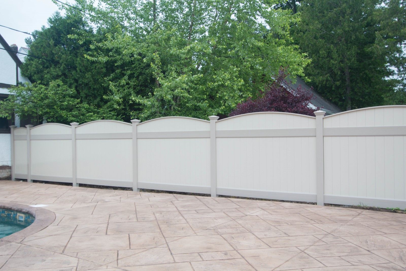 White vinyl privacy fence along a patio with green trees and shrubs behind it