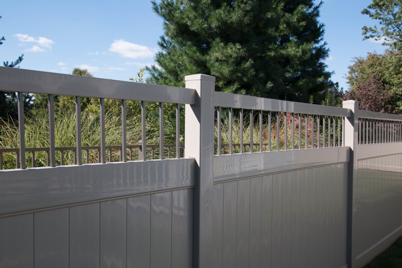 White vinyl privacy fence along a patio with green trees and shrubs behind it