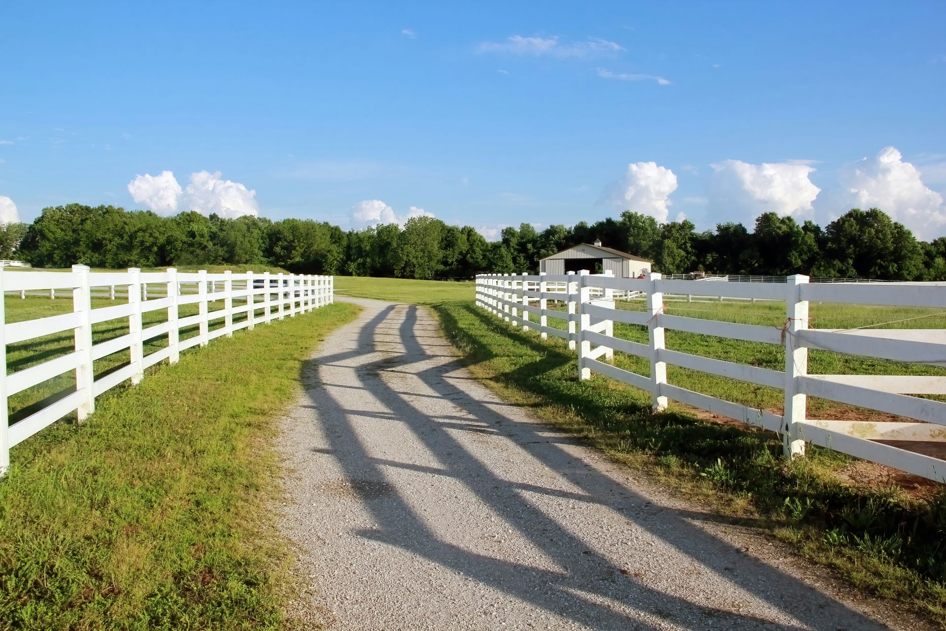 Gravel driveway lined with white fences leading to a house under a blue sky in Central PA