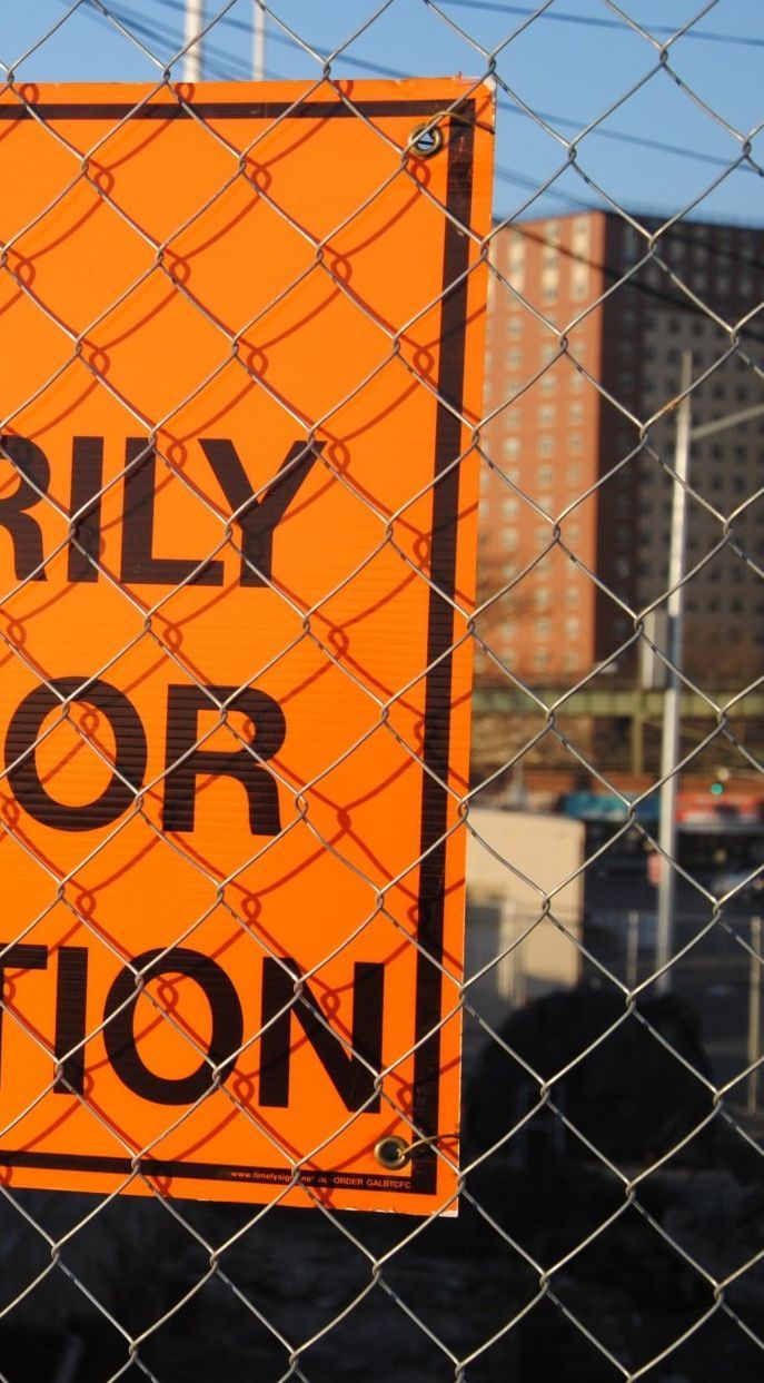 Orange construction sign behind chain-link fence, text visible: