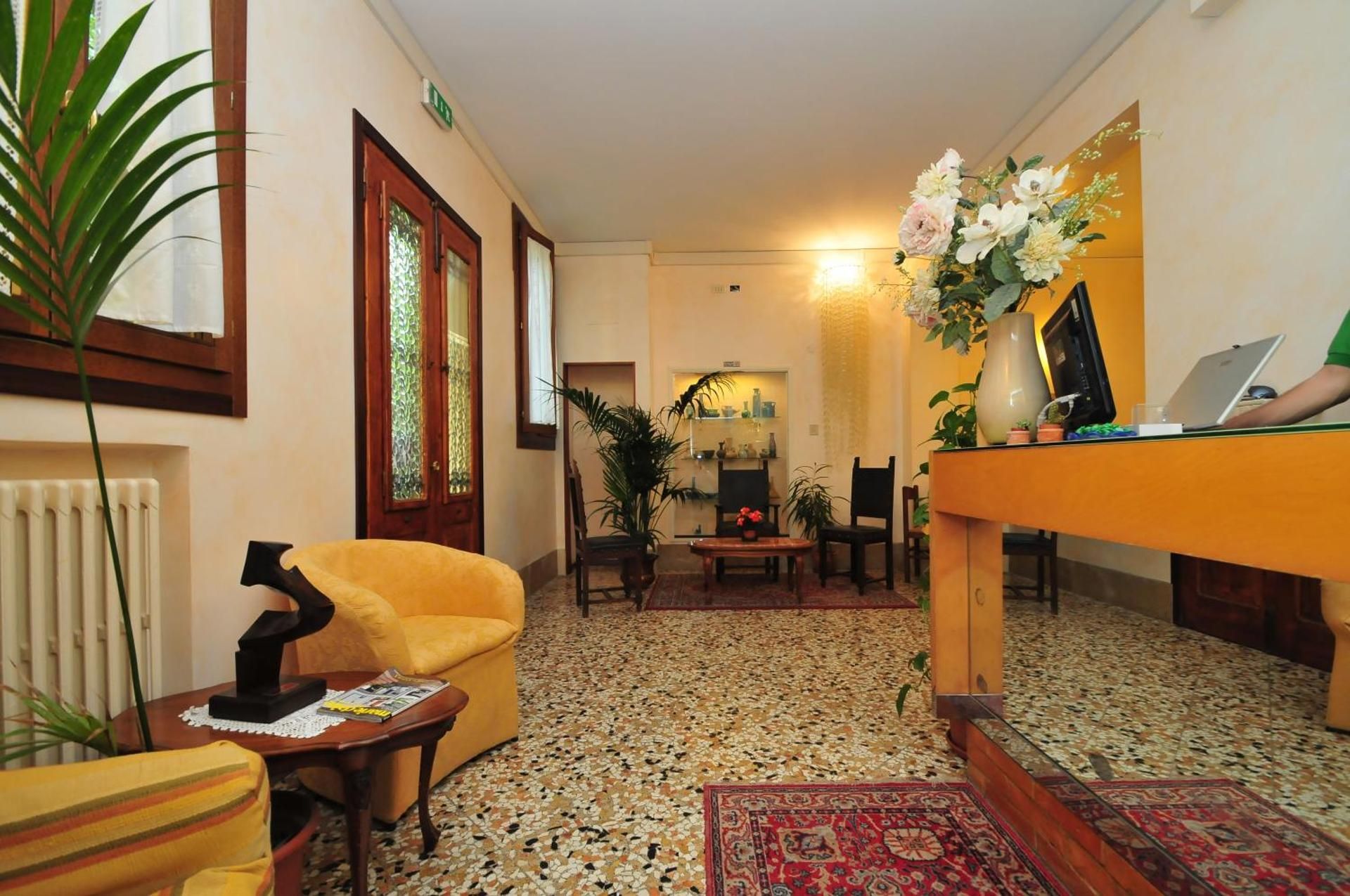Cozy living room with patterned rug, yellow armchair, wooden table, plants, and a hallway view