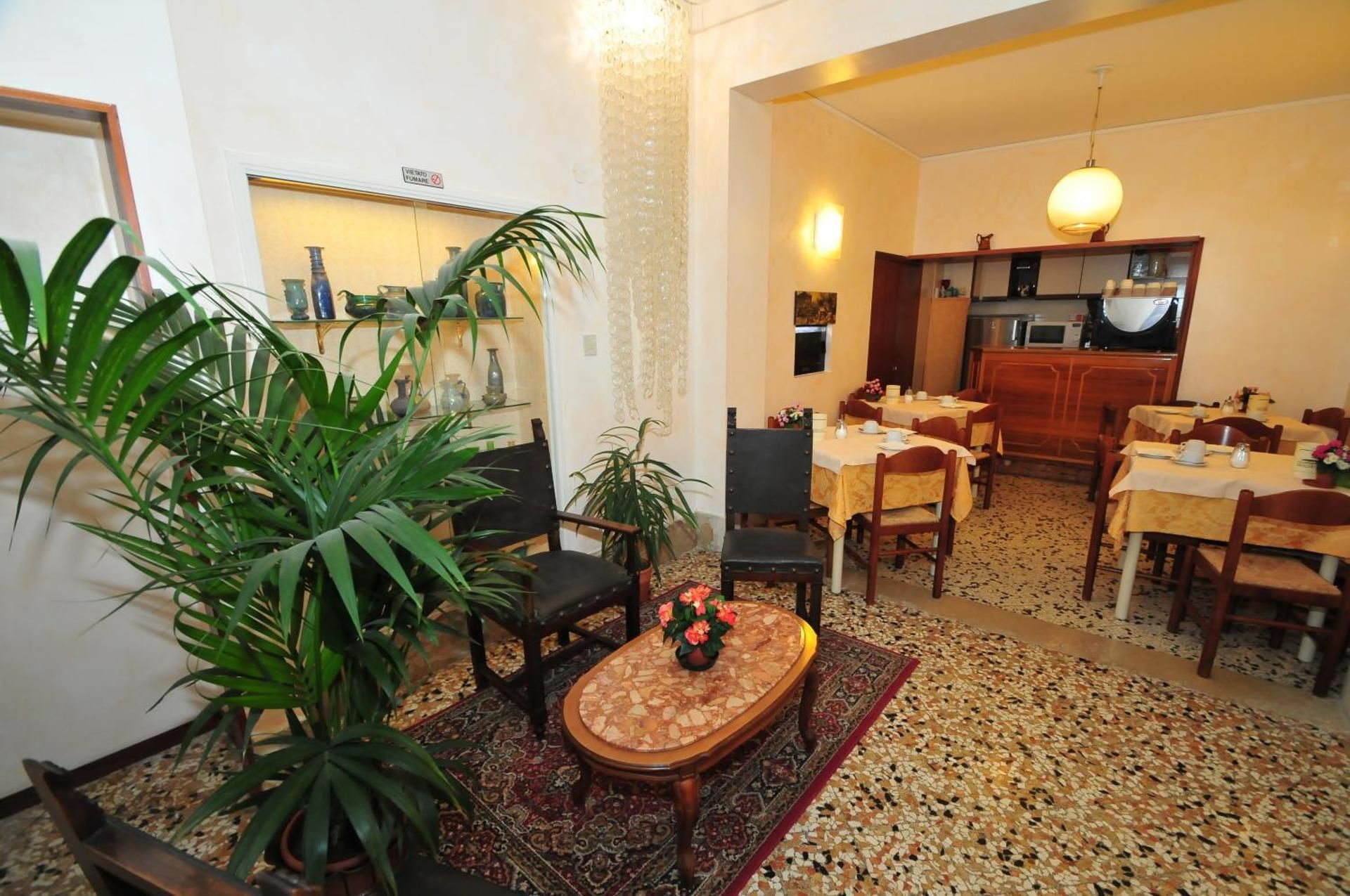 Cozy dining room with wooden tables, patterned rug, and large potted plants near a mirror.