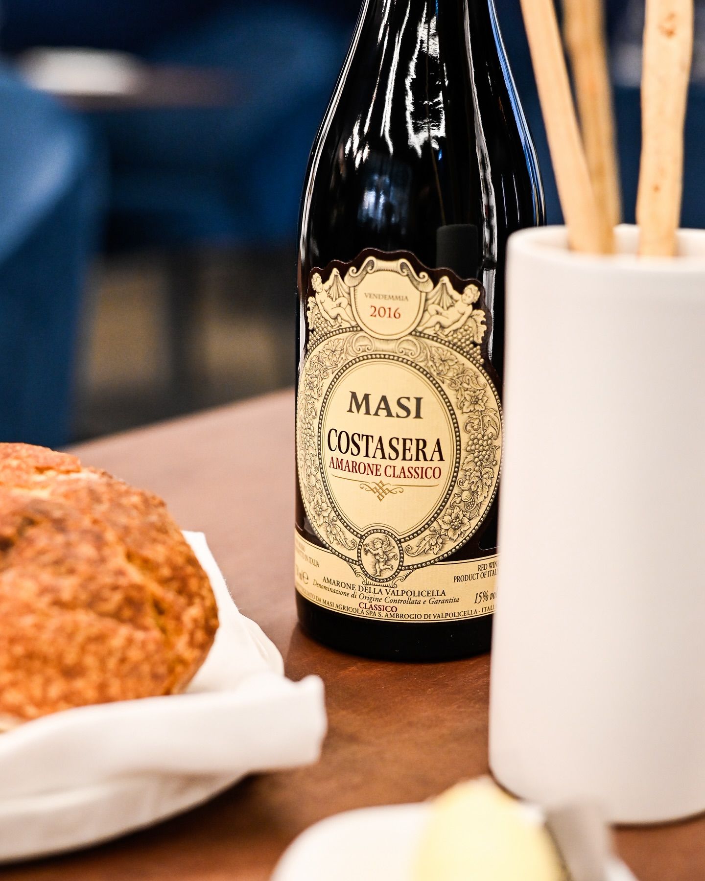Una bottiglia di vino Masi Costanera è appoggiata su un tavolo accanto a una pagnotta.