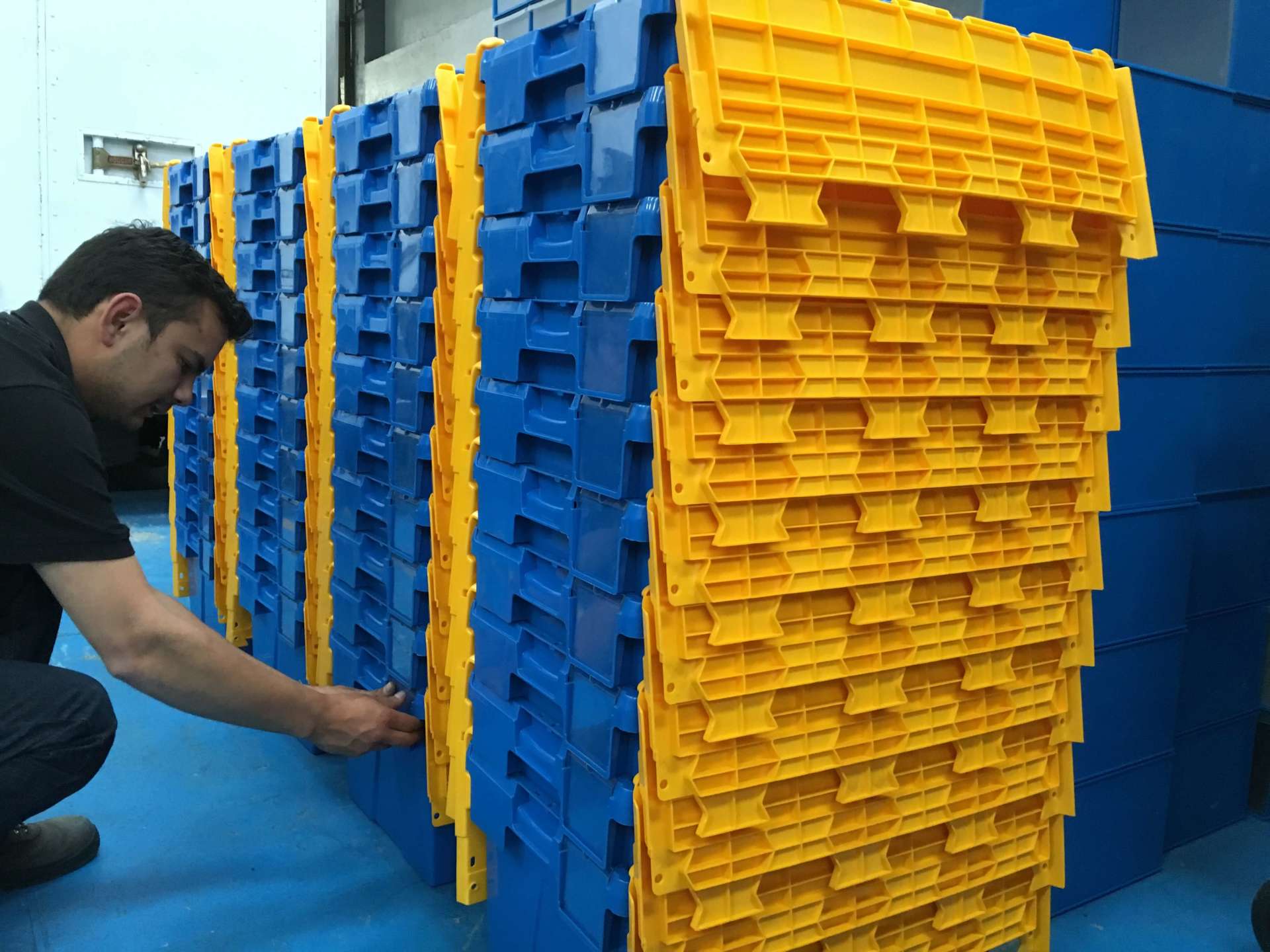 Un hombre está trabajando en una pila de cajas de plástico azules y amarillas.