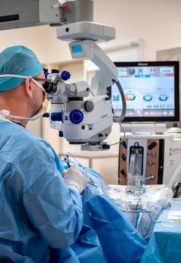 A surgeon is using a microscope in an operating room.