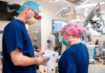 A surgeon and a nurse are in an operating room looking at a piece of paper.