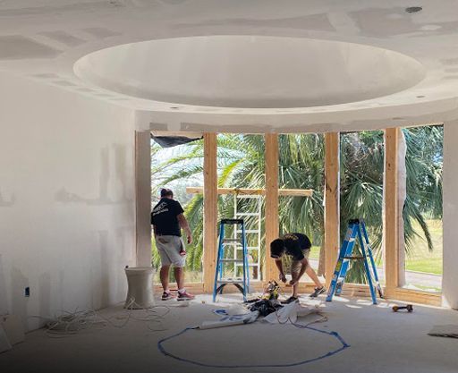 Two men are working on a ceiling in a room with a lot of windows.