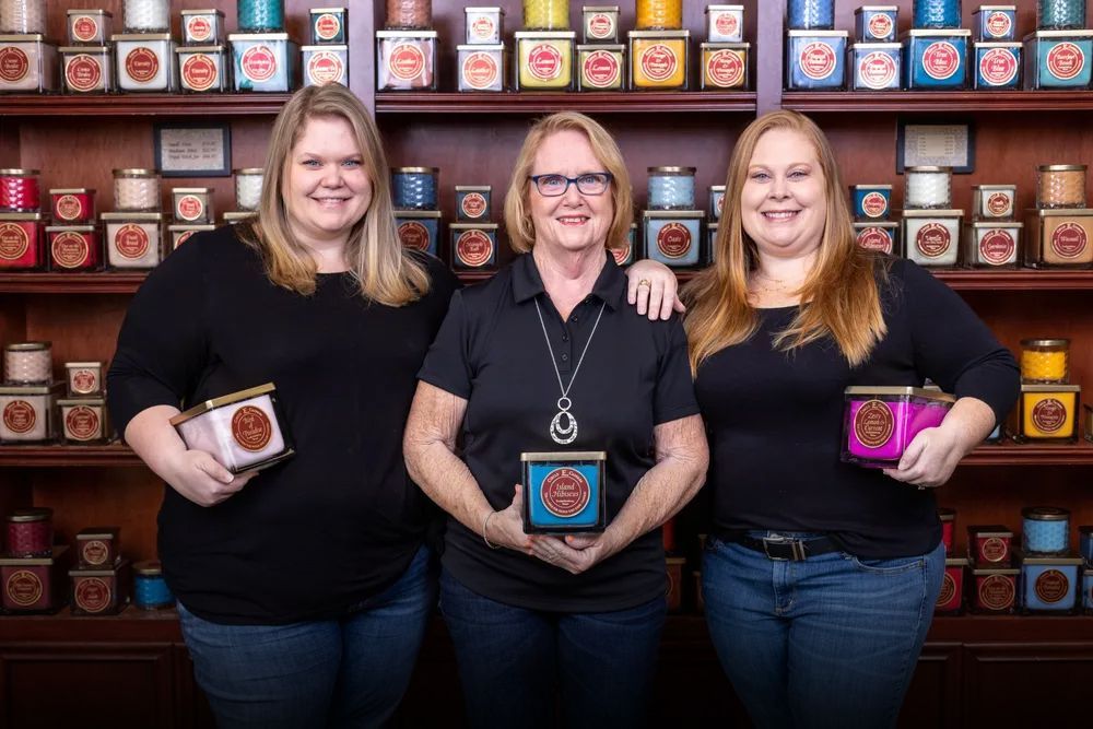 Three women are posing for a picture in front of a shelf of tea.