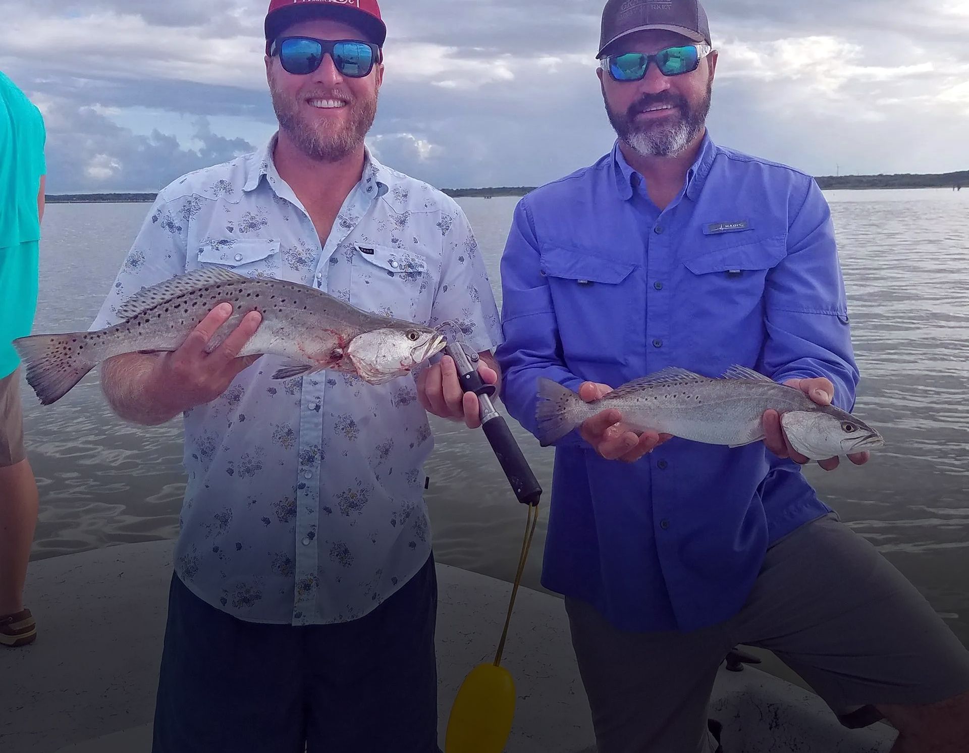 Two men are standing next to each other holding fish in their hands.