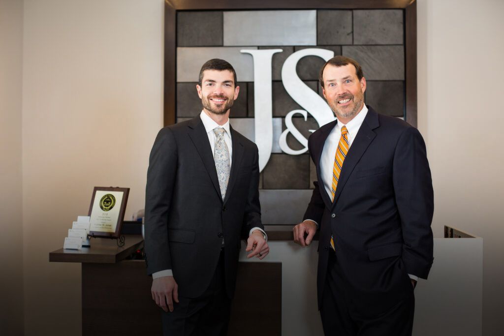Two men in suits and ties are standing in front of a sign that says j & s