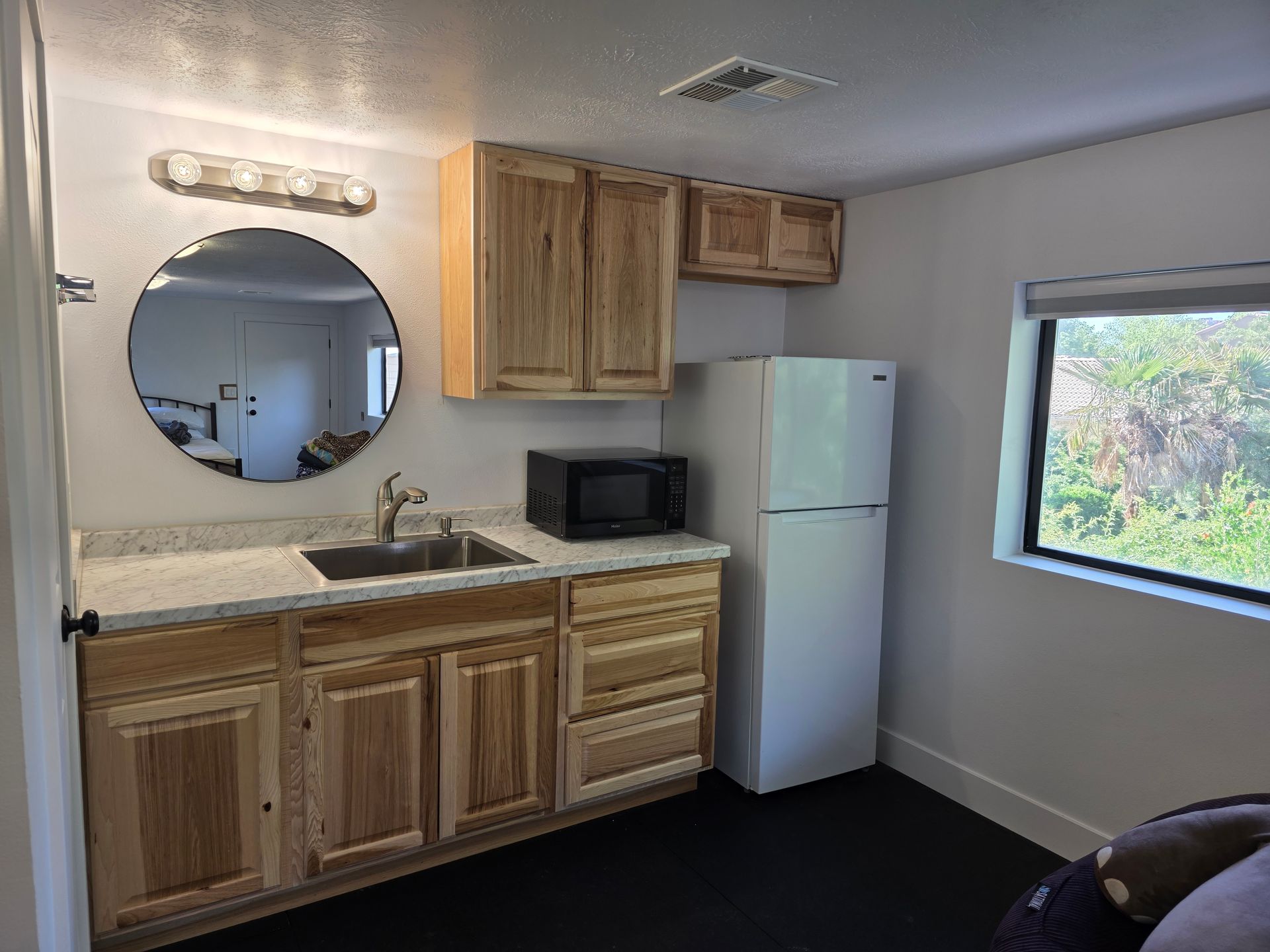 A kitchen with a sink , refrigerator , microwave and mirror.
