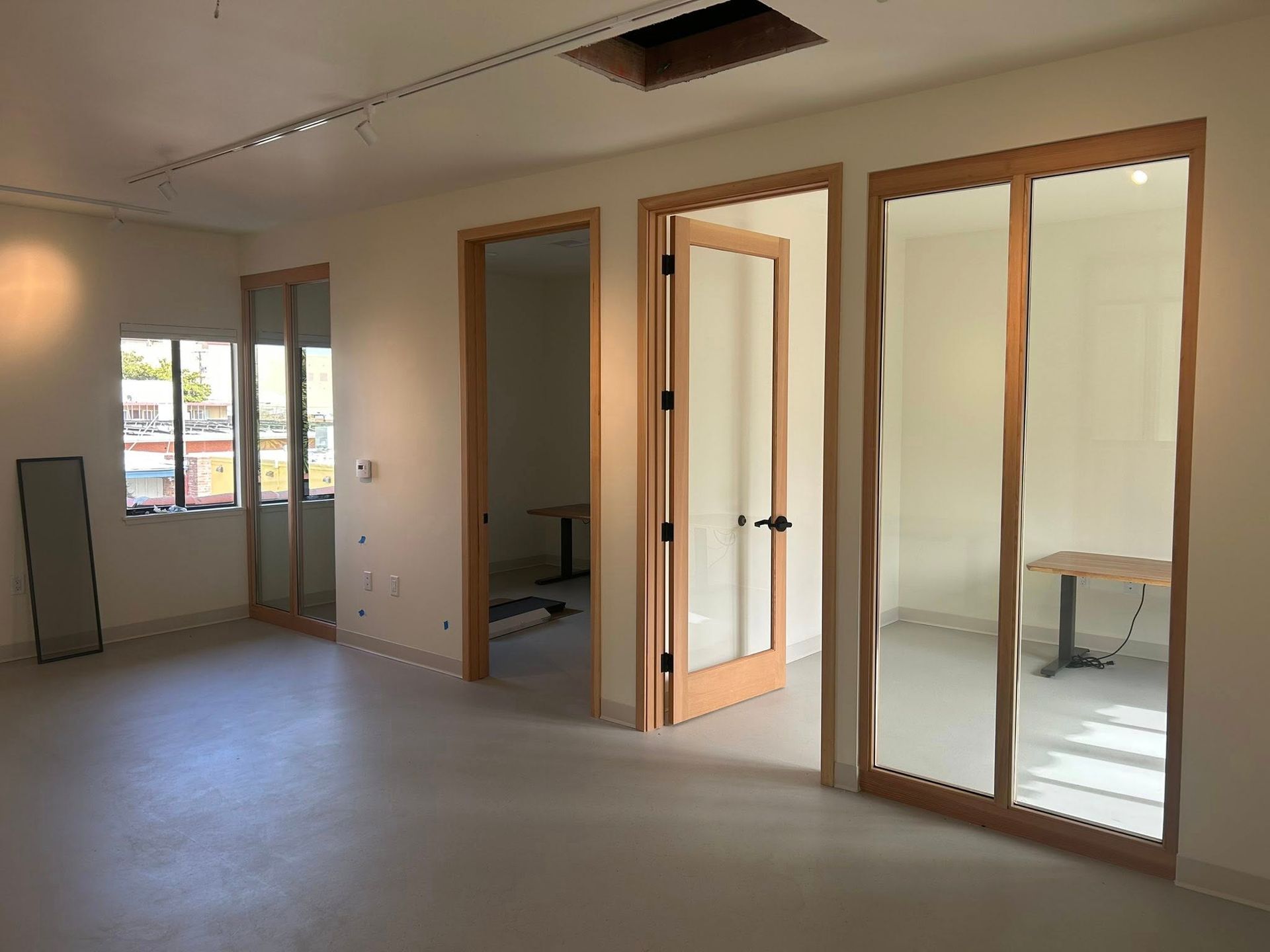 An office interior featuring white walls, a light gray floor, and three wooden-framed glass doors leading to small rooms.