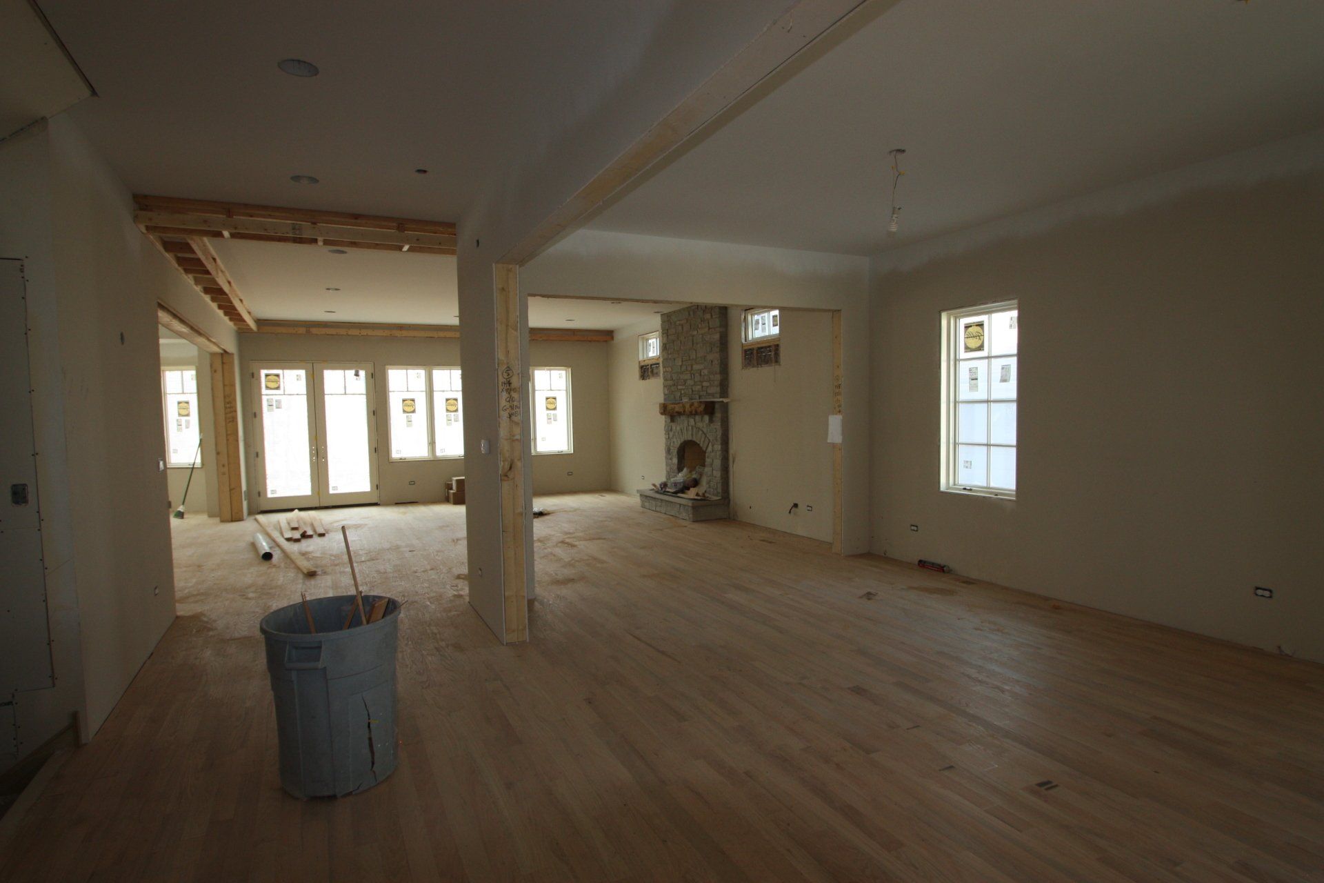 A large empty room with hardwood floors and a trash can in the middle.