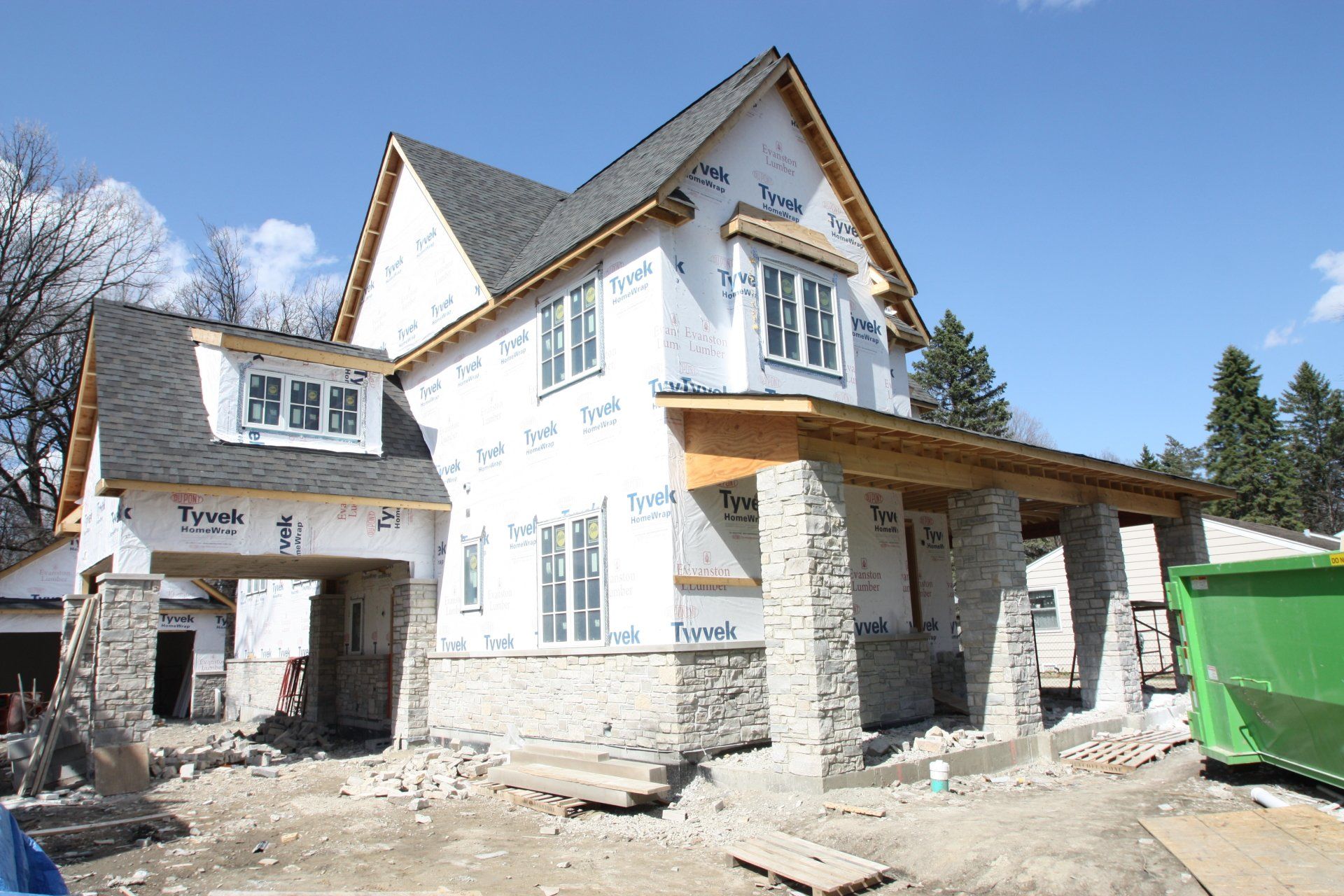 A house under construction with a green dumpster in front of it