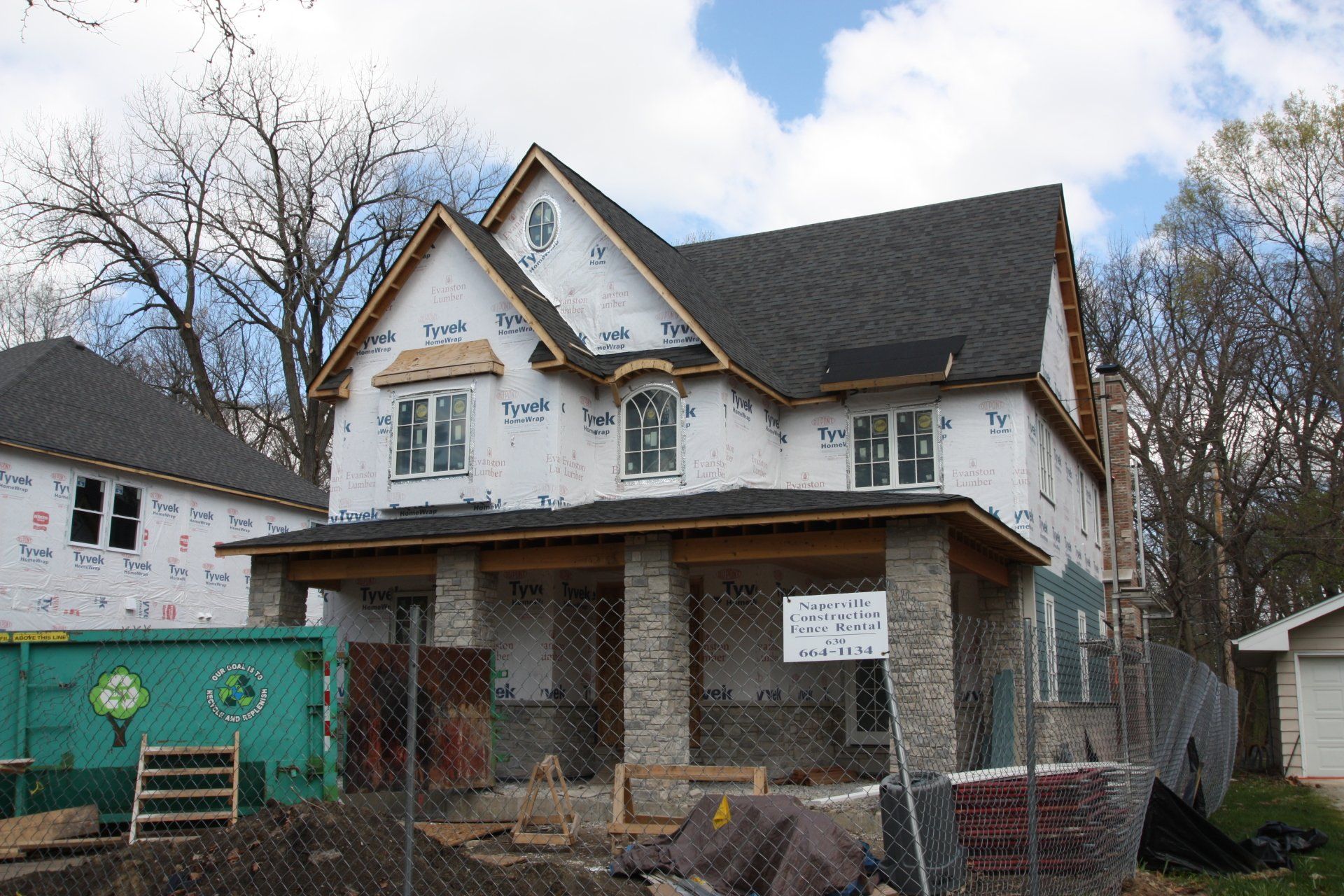 A house under construction with a green dumpster in front of it