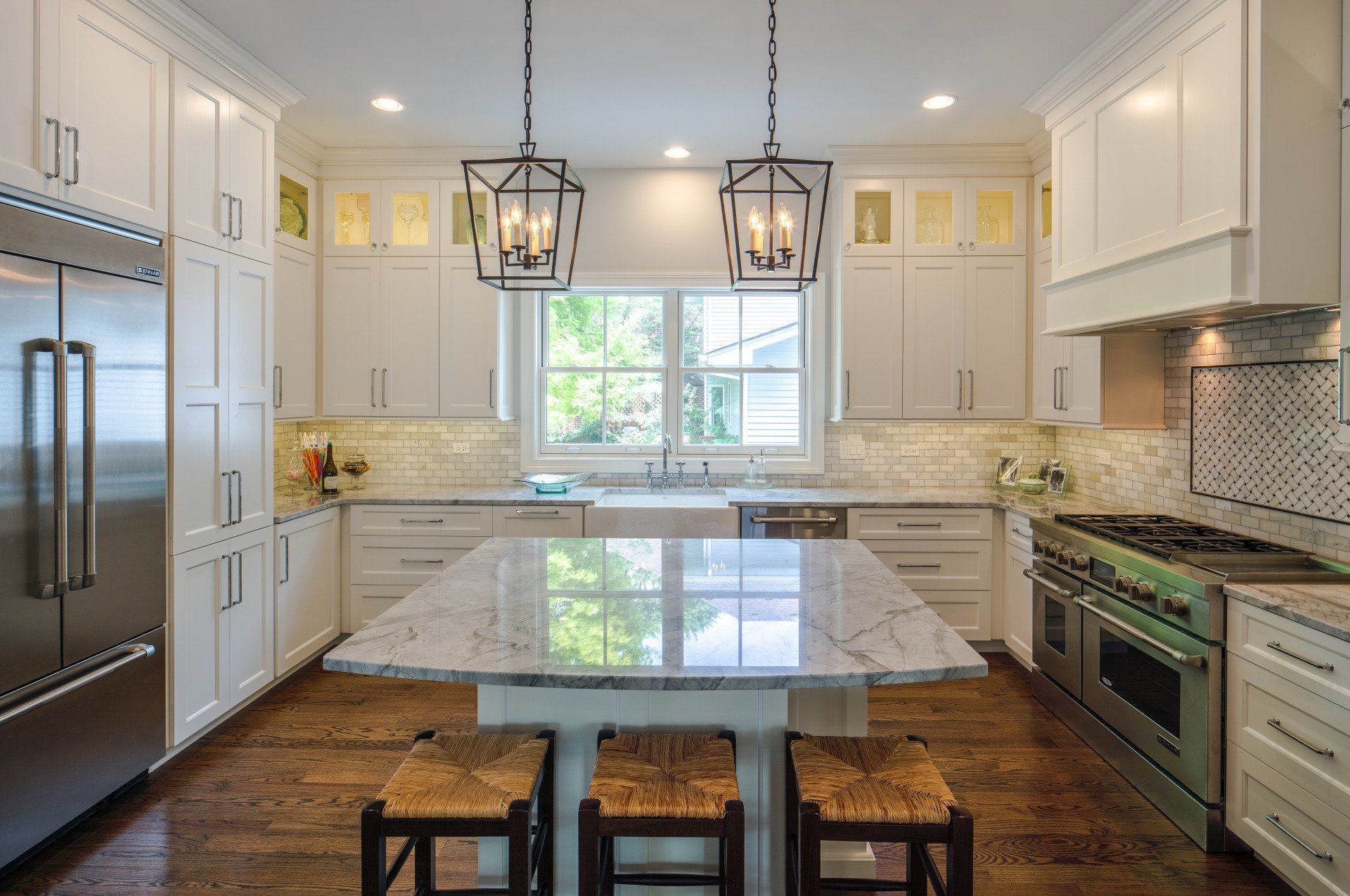 A kitchen with white cabinets , stainless steel appliances , a large island with a table and chairs.