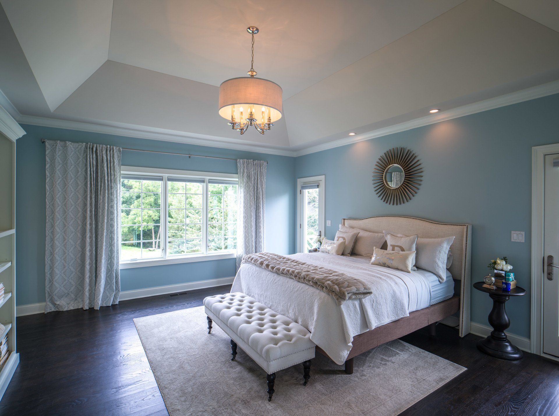 A bedroom with blue walls , a bed , a bench and a chandelier.